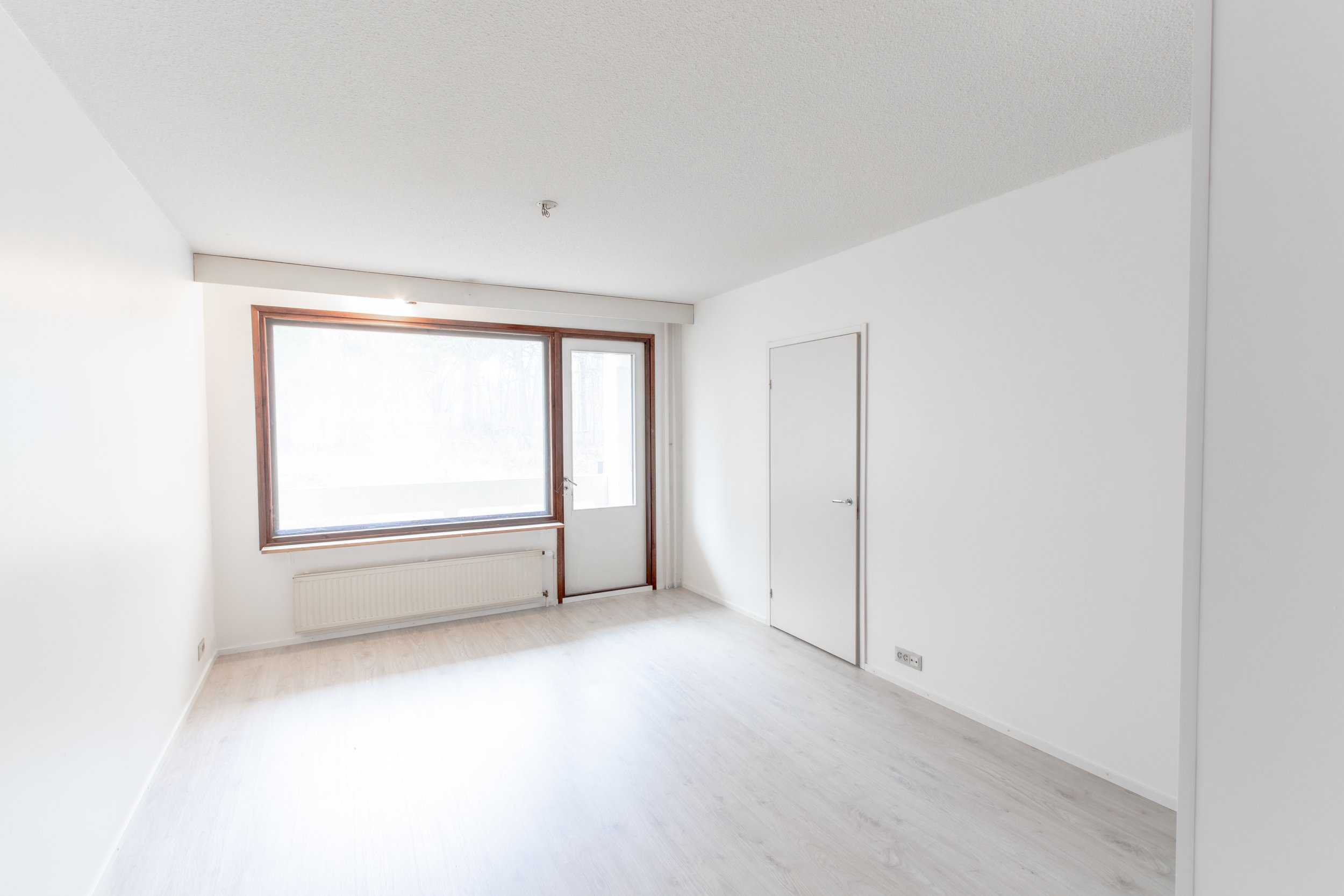 Tyhjä huone, jossa suuri ikkuna ja valkotiilinen lattia.