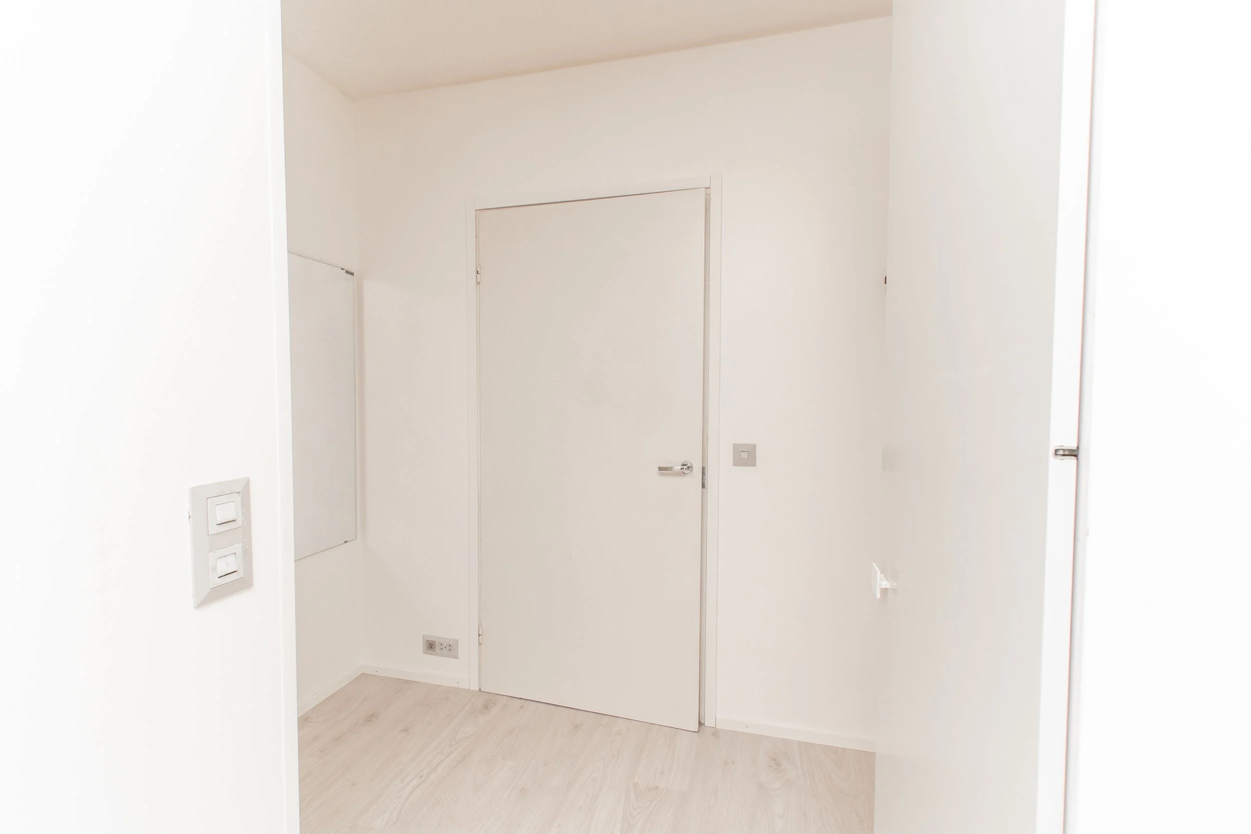 Tyhjä, valkoinen huone, jossa ovi ja sähköpistokkeita.