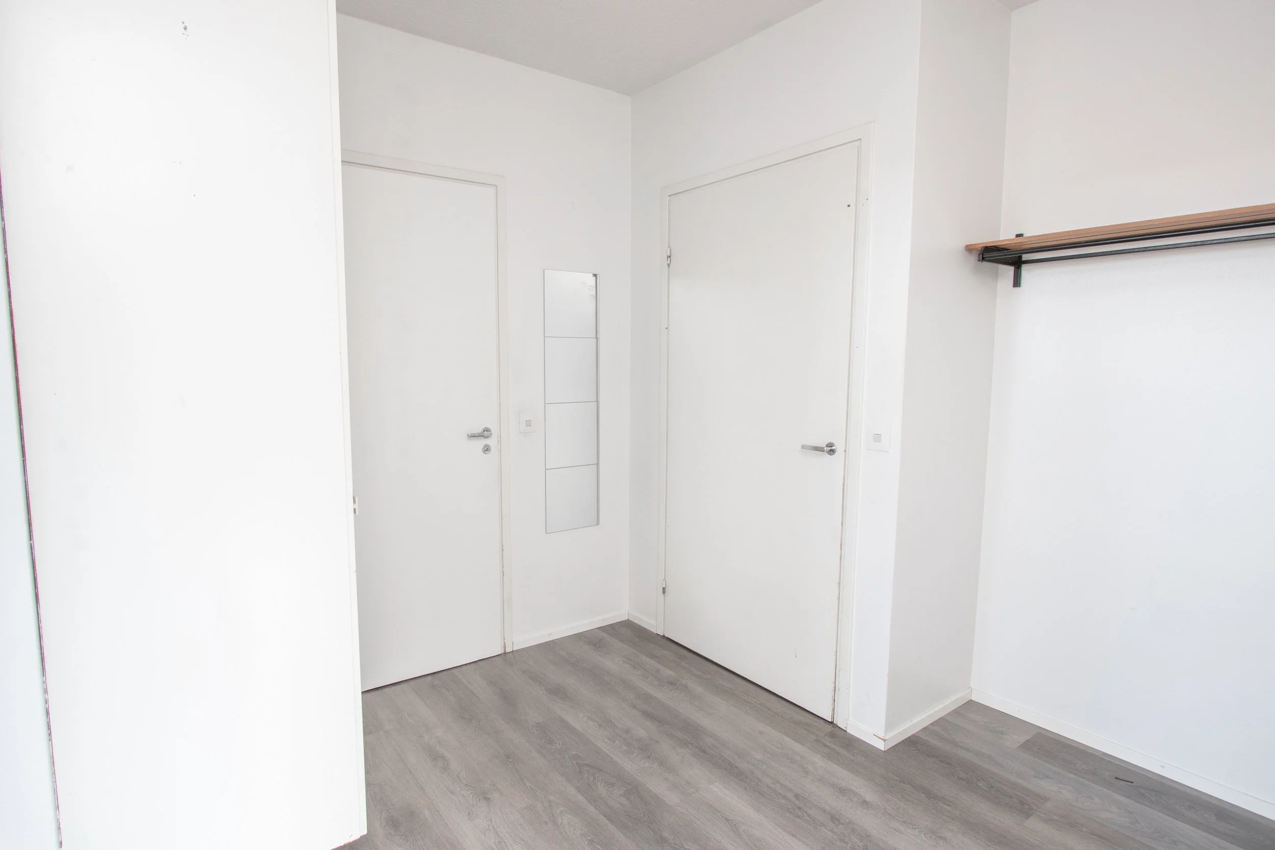 Tyhjä huone, valkoiset seinät, harmaa lattia, kaksi ovea ja pari seinähyllyä