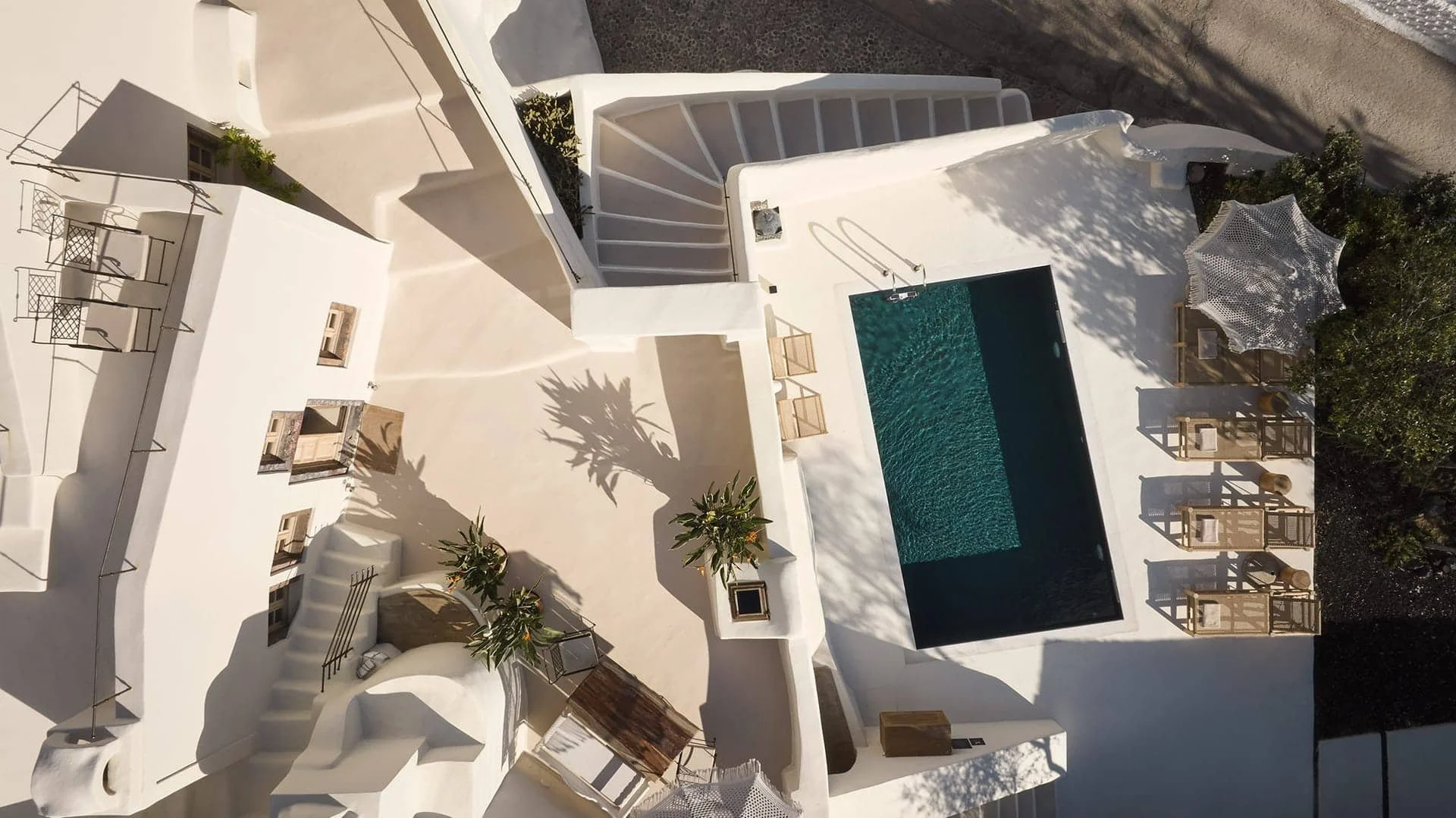 Vue aérienne d'une maison blanche avec une piscine bleue, des parasols, des chaises longues et des plantes.