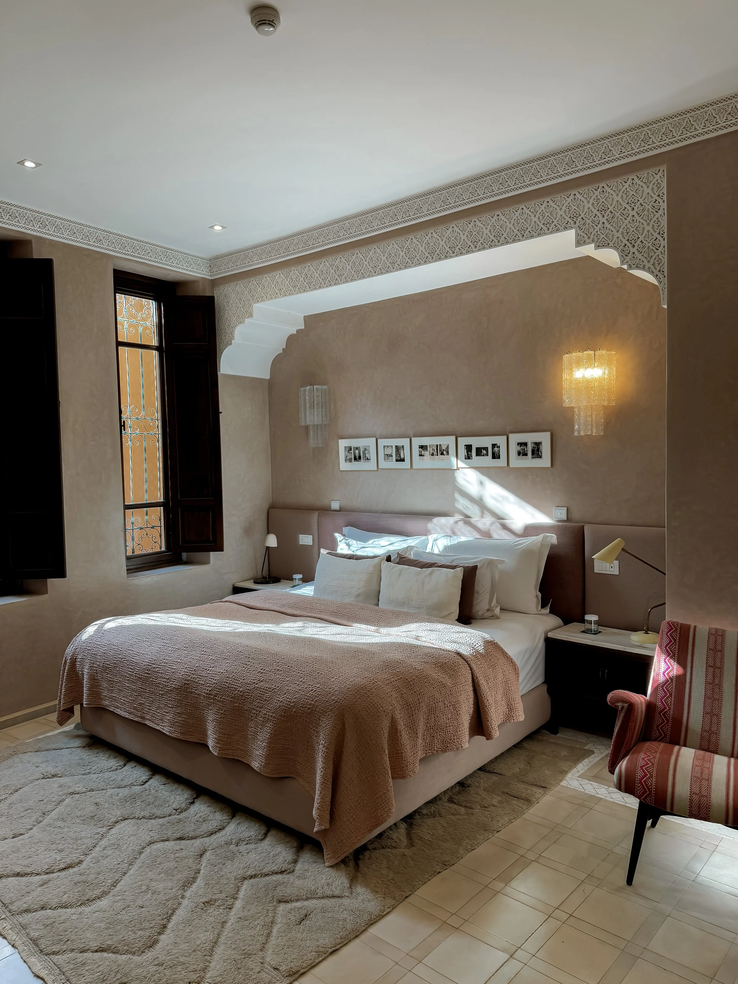 Chambre avec lit double, rideau avec volets en bois, tapis beige, lampes, tableau de photos.
