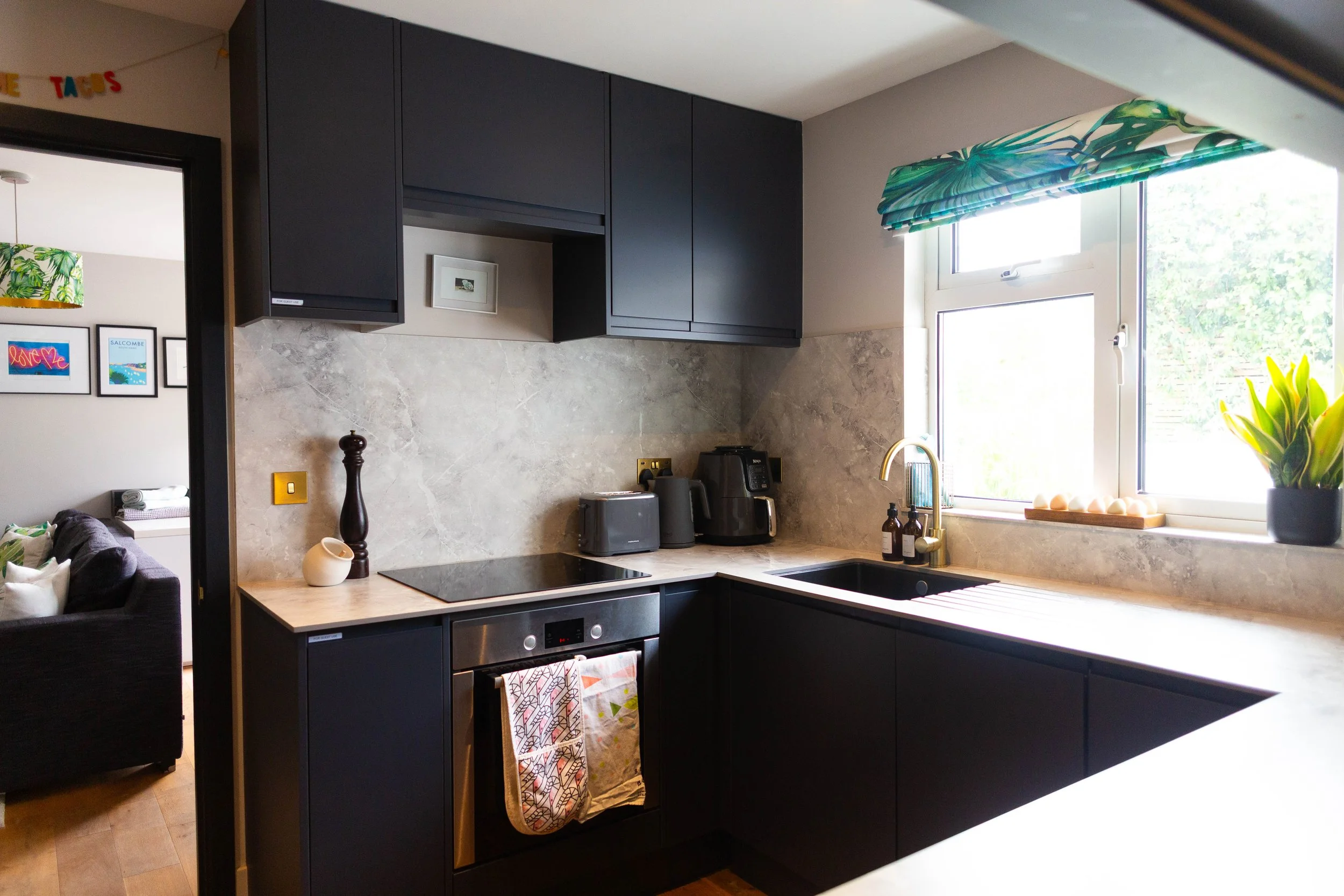 Modern kitchen with black cabinets, marble backsplash, window with green leafy valance, and kitchen appliances on countertop.