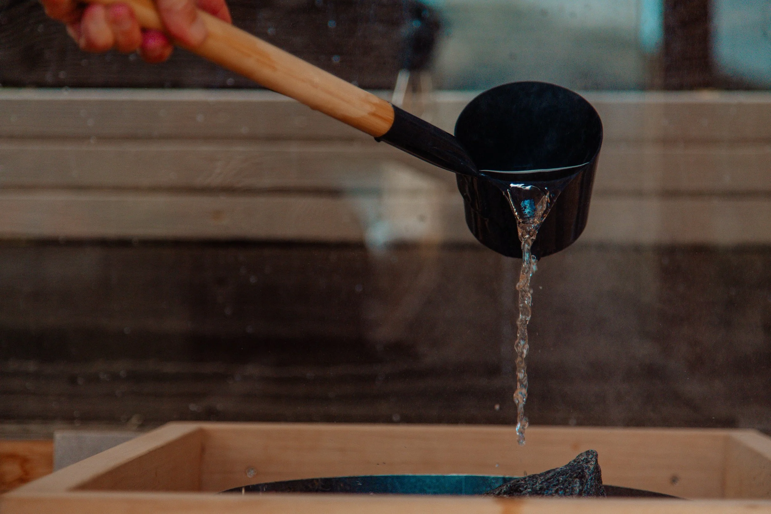 A hand holding a black scoop with water pouring out into a wooden container.