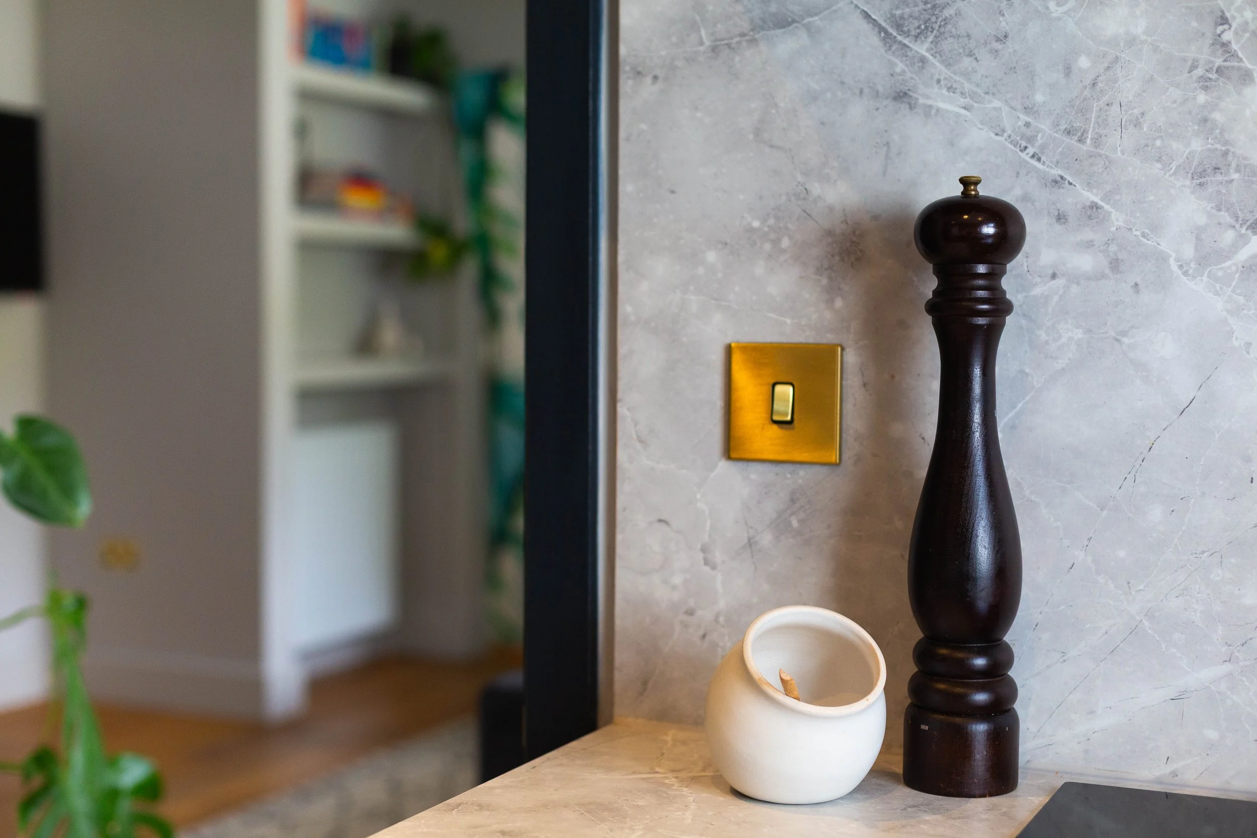 Decorative arrangement of a tall dark wooden vase and a shorter white ceramic vase on a marble surface, with a gold light switch and a mirror reflecting a blurred bookshelf in the background.