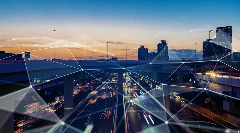 City highway at sunset with multiple levels of overpasses and high-rise buildings in the background, overlaid with digital network lines.