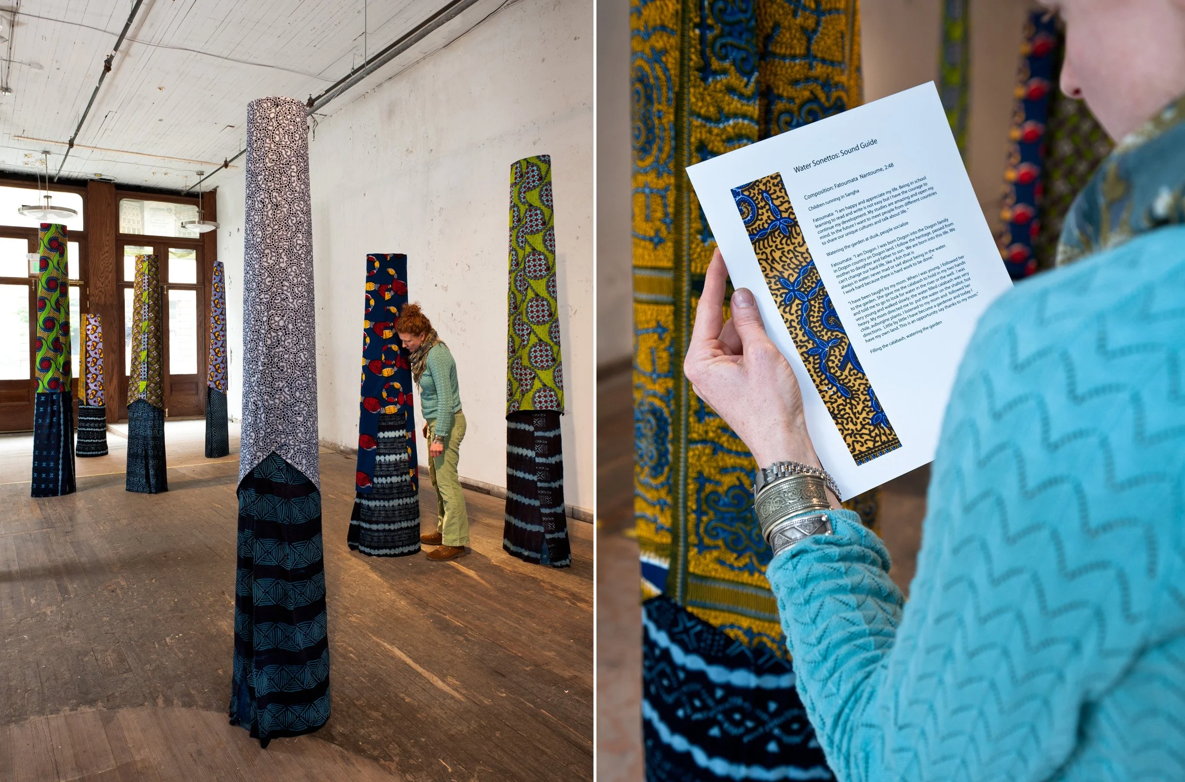 A woman leans in to listen to one of the elliptical columns that makes up part of the installation SOURCE - They covered in wax resisted and indigo dyed West African textiles that are arranged about the gallery.