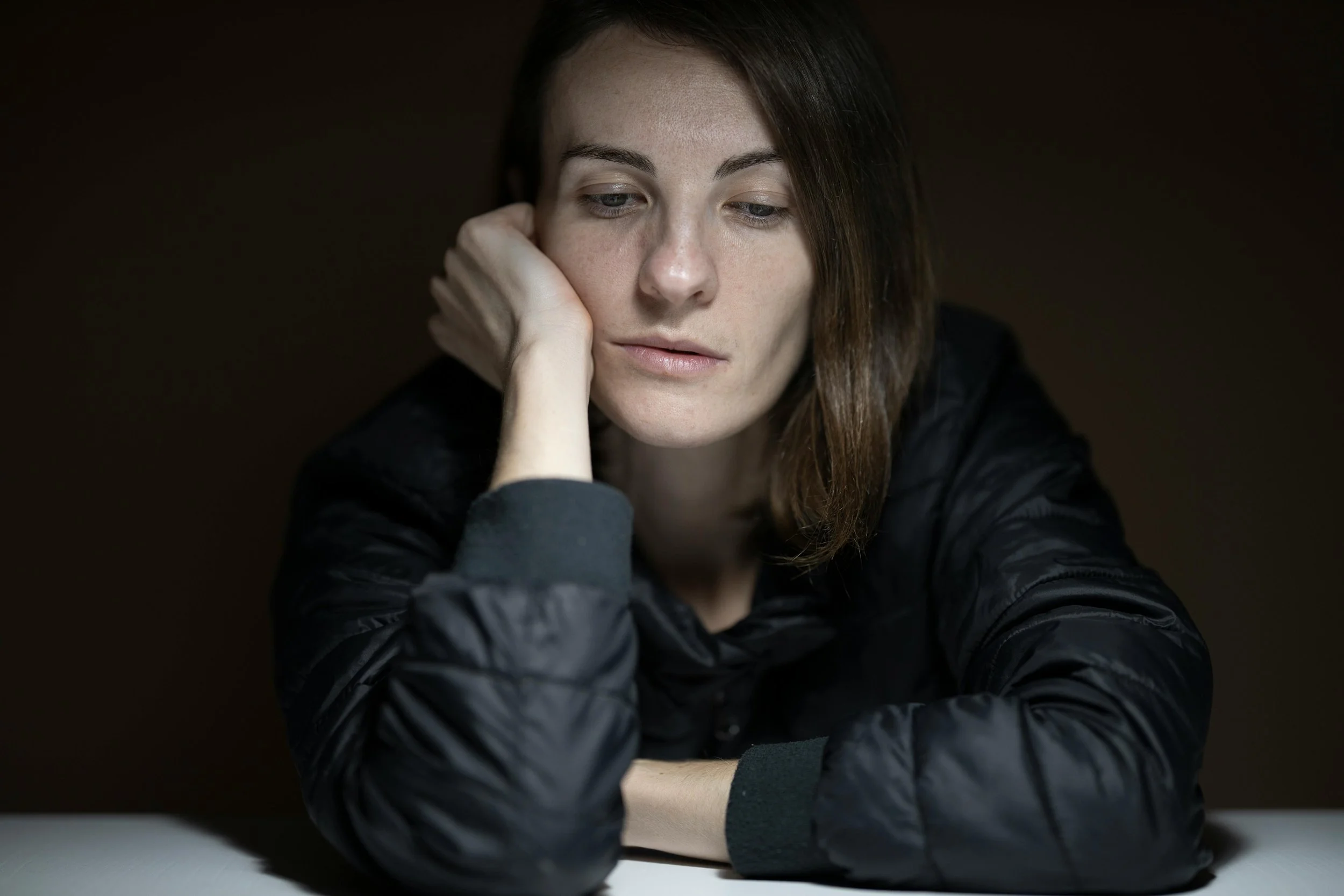 woman sitting at table in dark looking sad