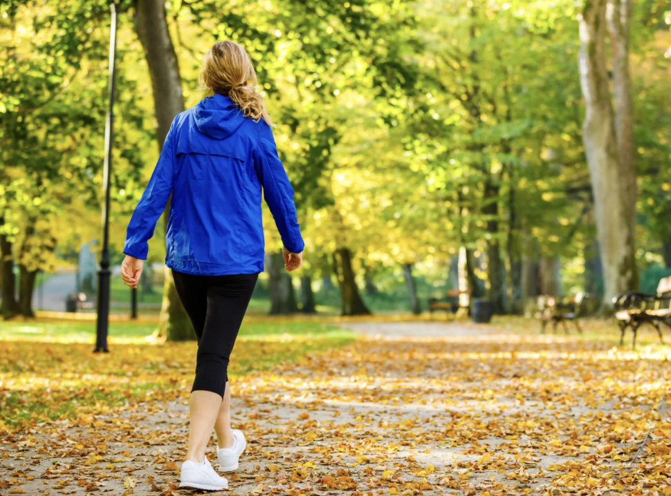 woman walking on leaf covered path in park