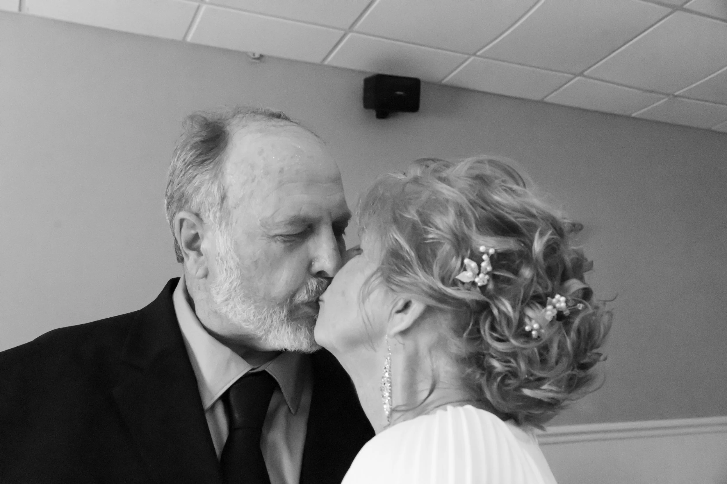 An elderly man and woman share a kiss in a black-and-white photo.