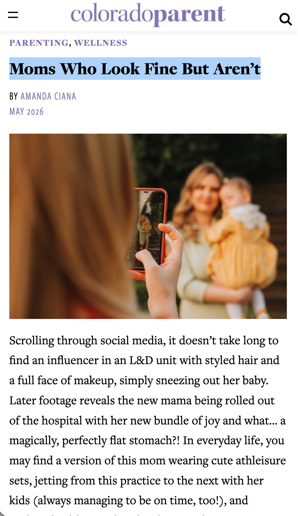 A woman holding a baby dressed in yellow is being photographed by another person using a smartphone; the woman and baby are smiling.