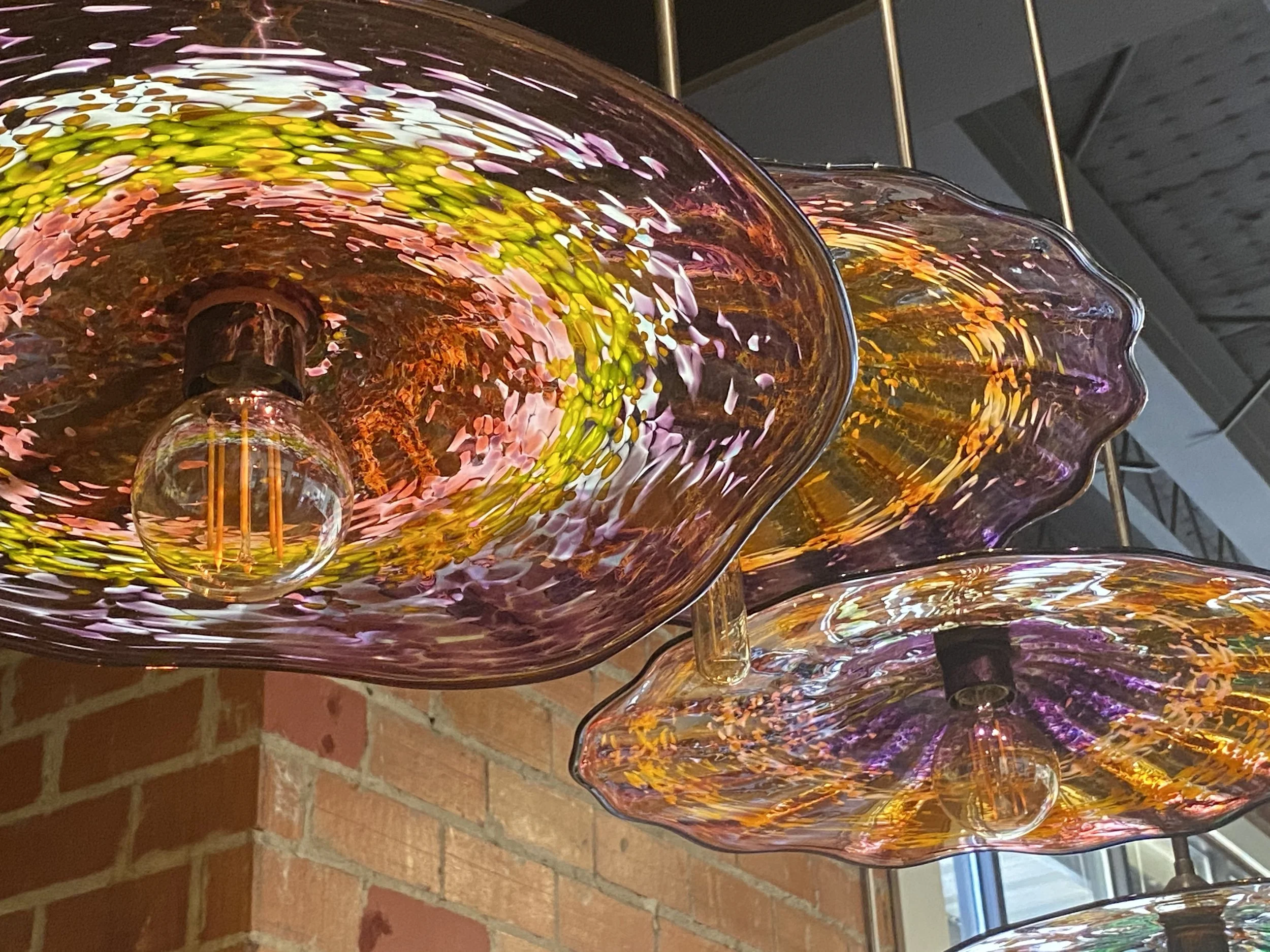 Colorful paper lantern hanging from ceiling in a mostly black and white dining room with a table, four chairs, potted plant, wall clock, window with blinds, and a fruit-themed painting on the wall.