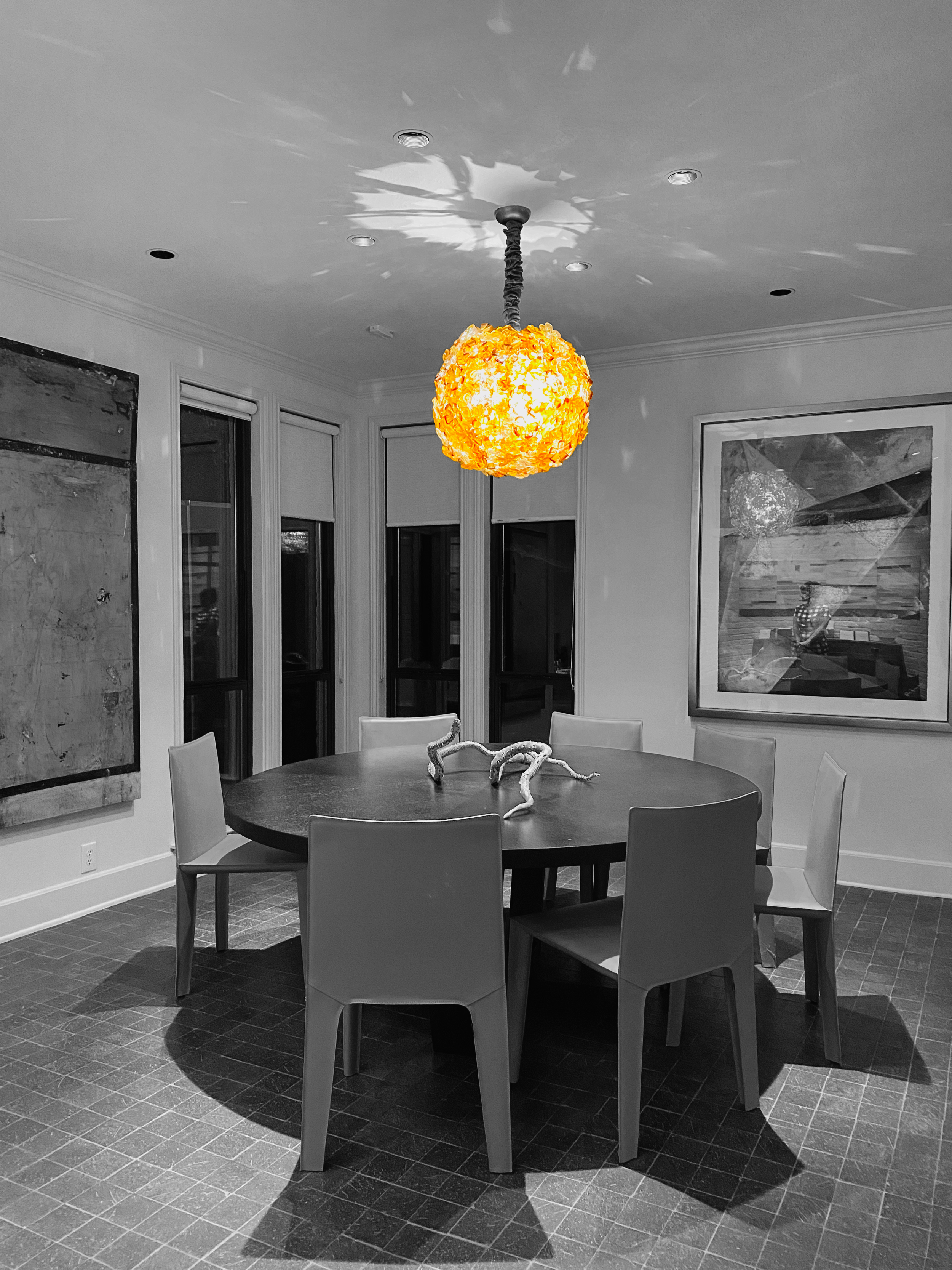 A dining room with a round table and six chairs under a vibrant orange hanging lamp, with black-and-white walls and artwork.