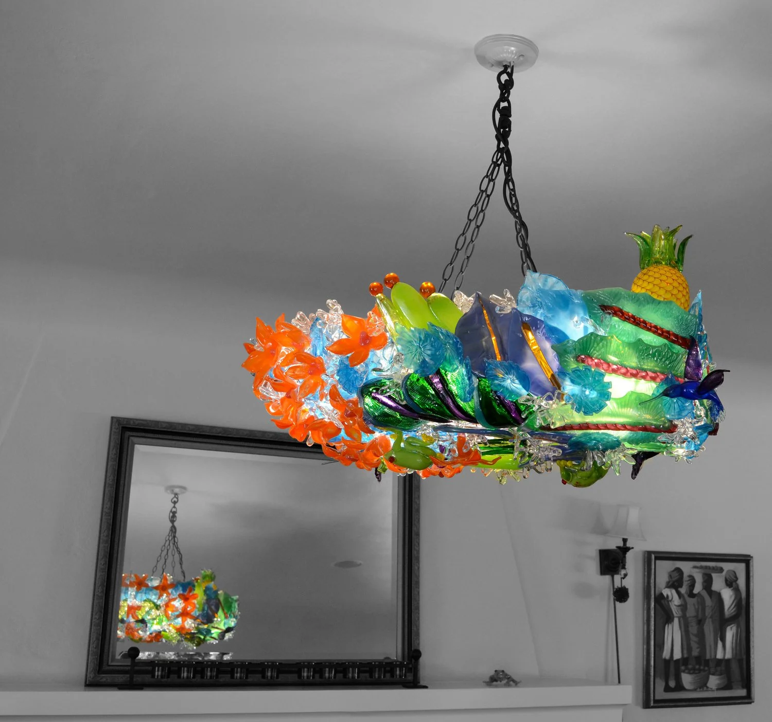 Colorful glass chandelier with tropical fruit and floral design, reflecting in a mirror on a wall.
