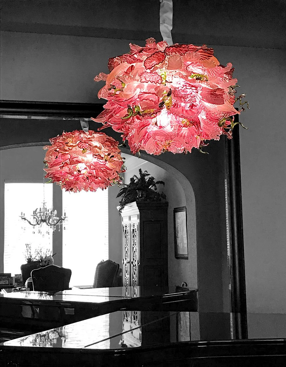 Two pink flower-shaped hanging lamps in a black-and-white dining room, with a high-back chair and a chandelier in the background.