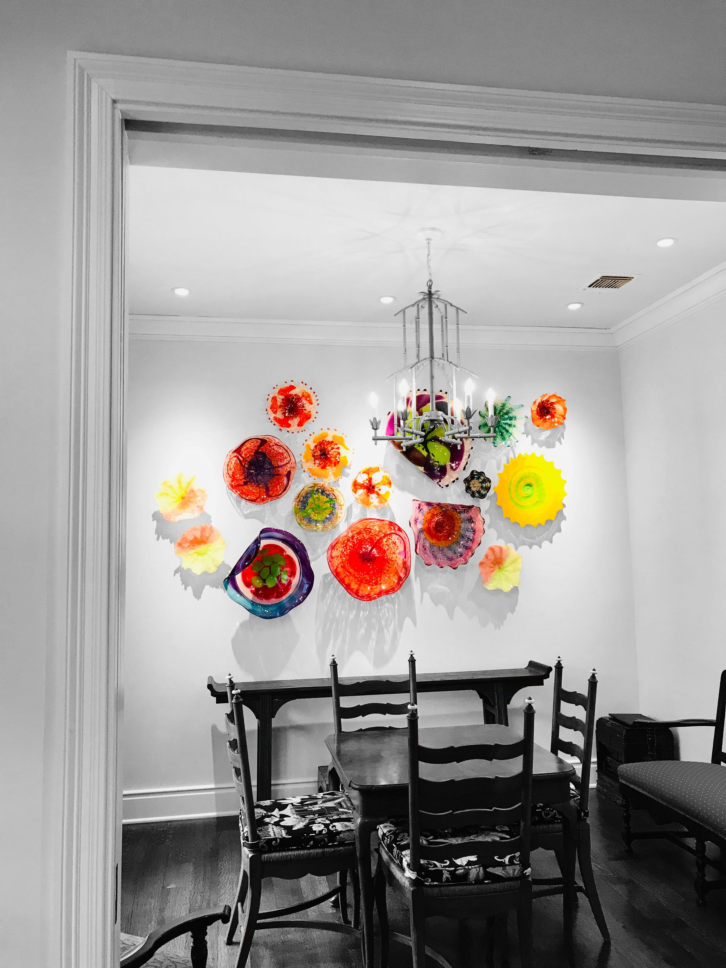 A dining room with a chandelier and a wall decorated with colorful, abstract glass art pieces.