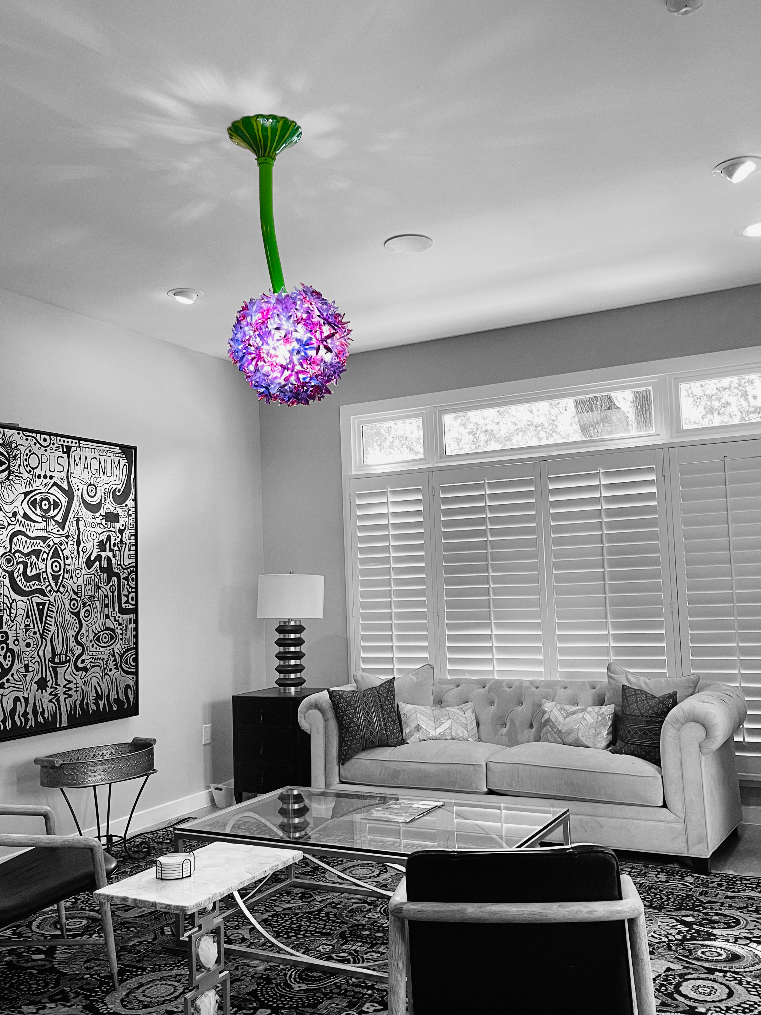 Colorful hanging light fixture resembling a flower in a black and white living room with a cream tufted sofa, framed artwork, and various chairs.