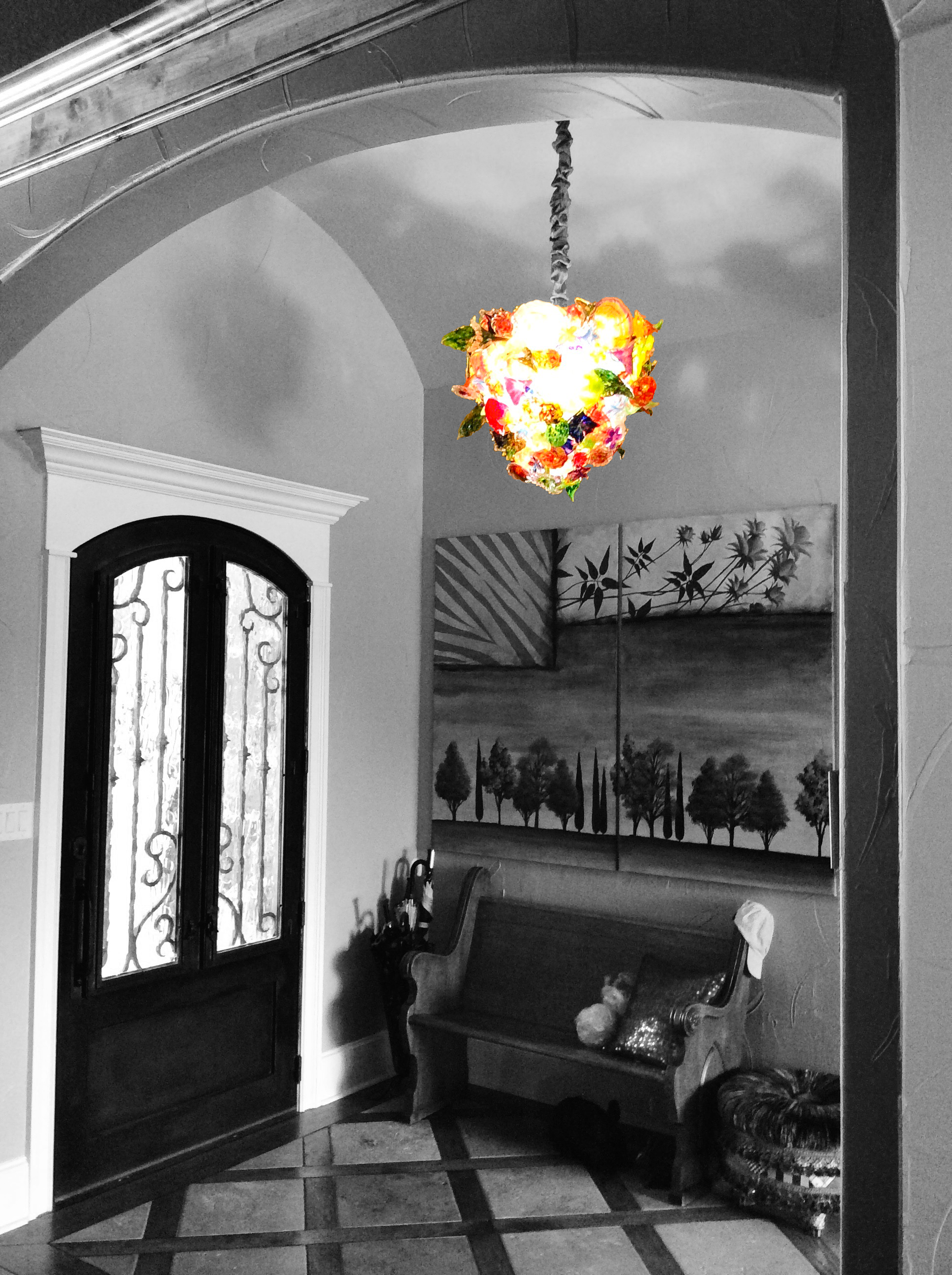 Interior of a house with a black and white color scheme, featuring a decorated front door with ironwork, a wooden bench with pillows, and a colorful floral chandelier hanging from the ceiling.