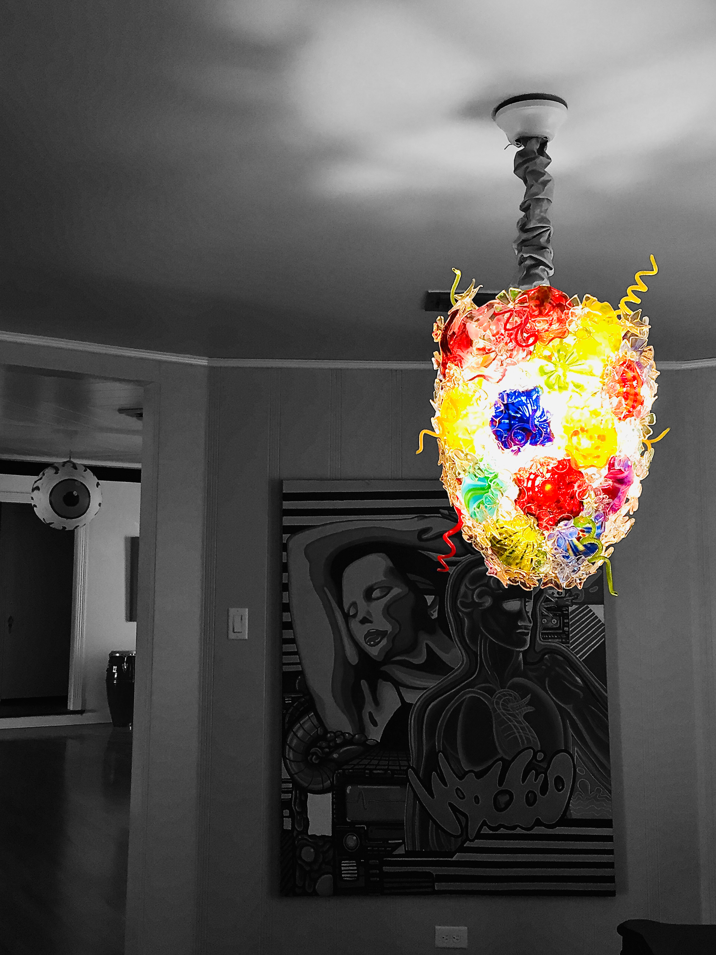 Colorful, decorated hanging lampshade in a room with black-and-white wall art.