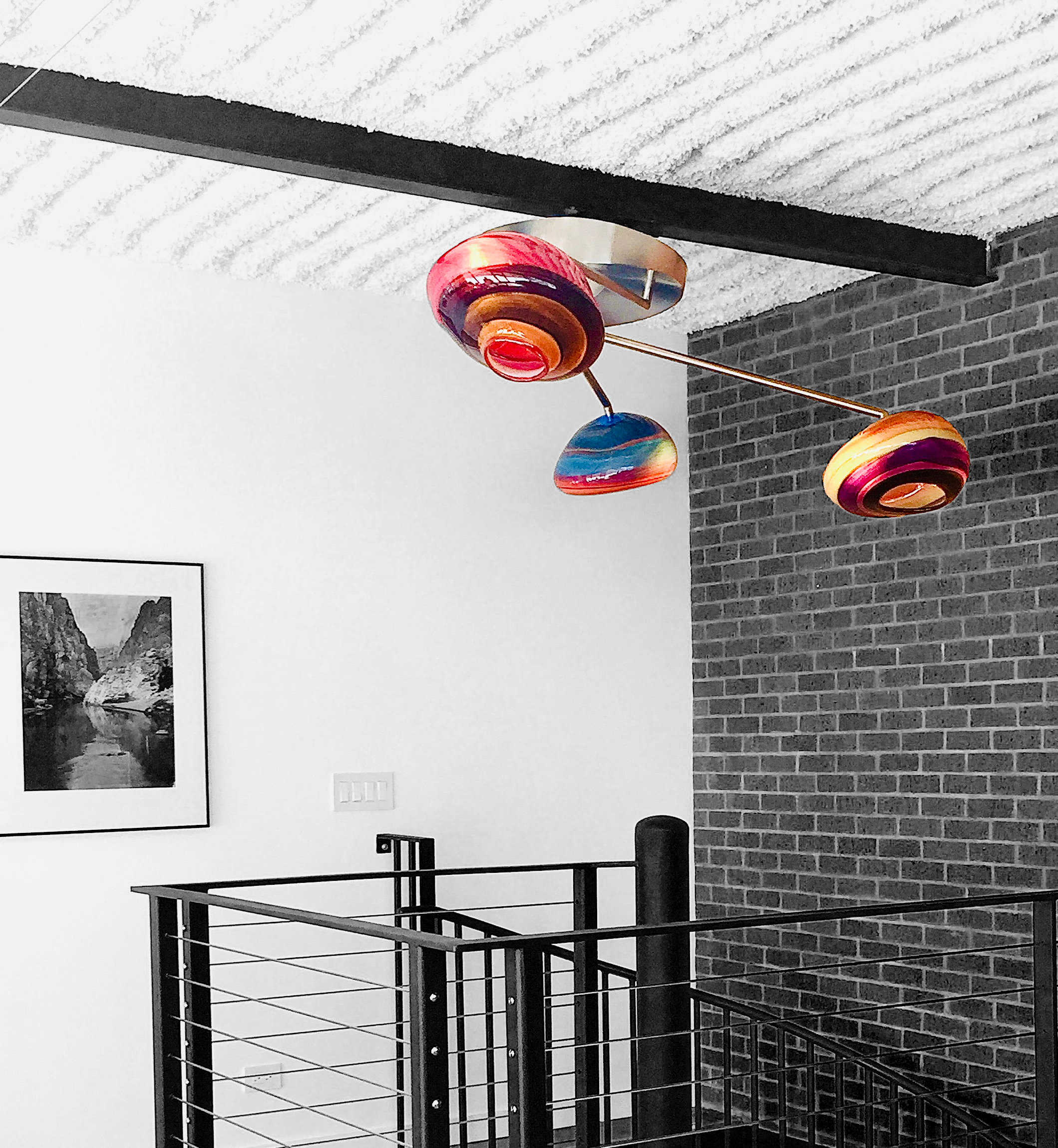Colorful modern chandelier with round, multicolored glass orbs hanging indoors against a white wall and brick accent wall.