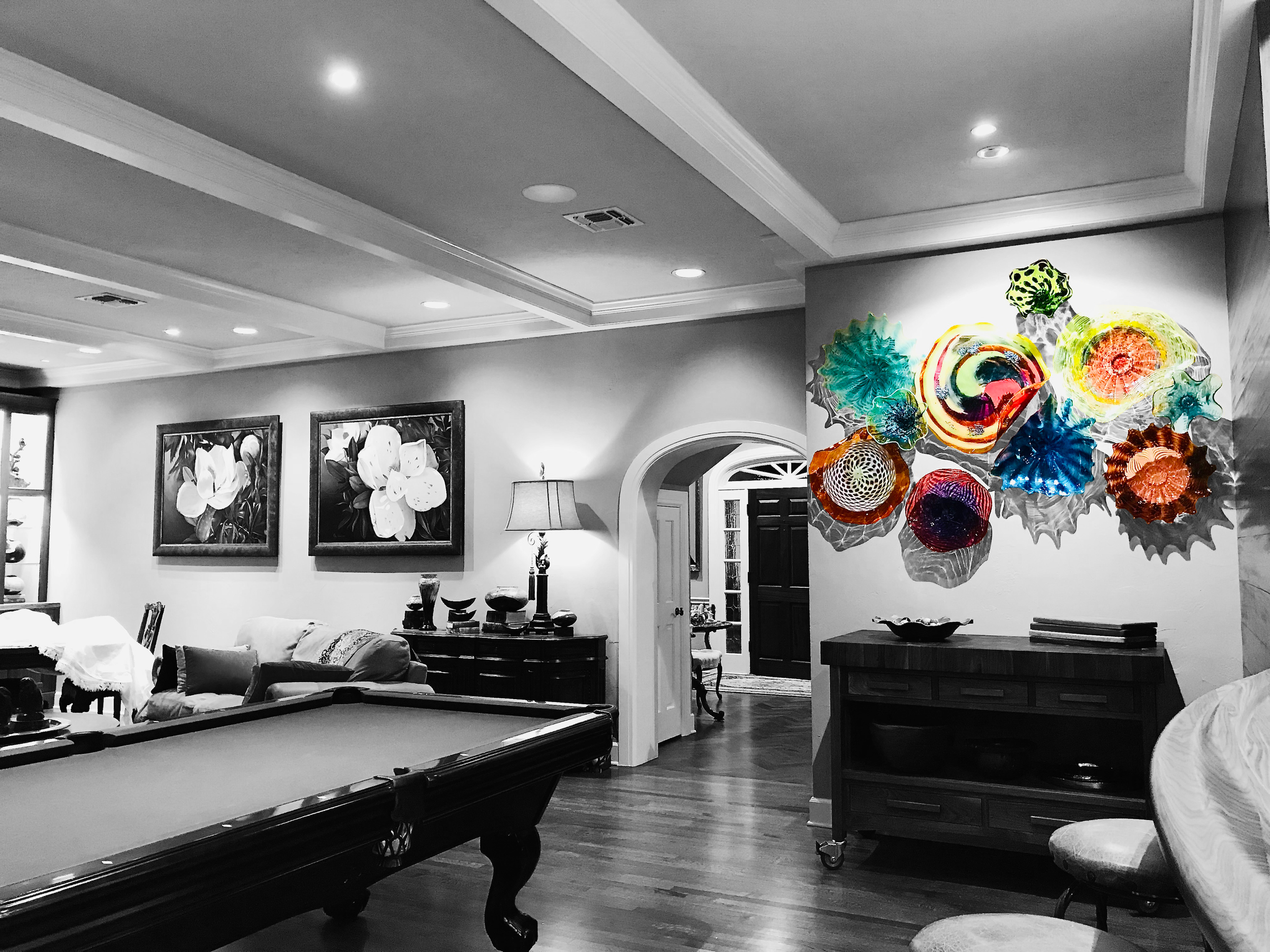 Living room with black and white floral artwork on the wall, a pool table, and a colorful glass art installation on the wall.