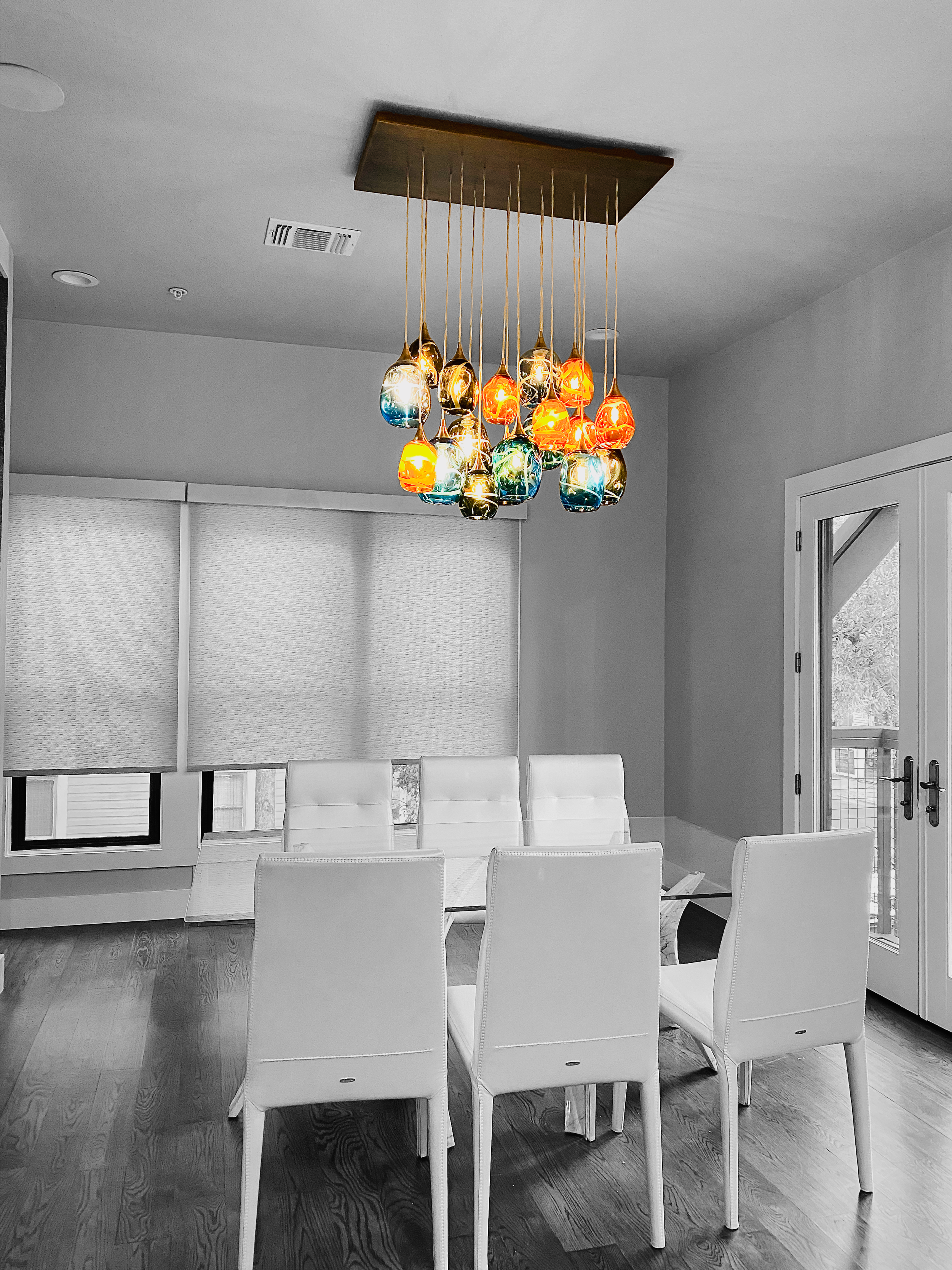 Colorful modern pendant light hanging above a white dining table with six white chairs, with the rest of the image in black and white.