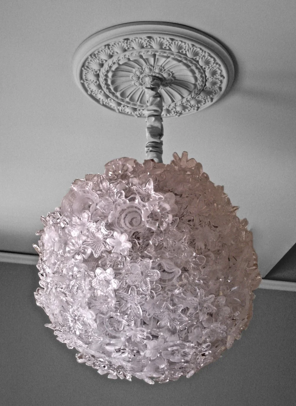 Pink glass chandelier with floral and butterfly shapes hanging from a decorated ceiling medallion.