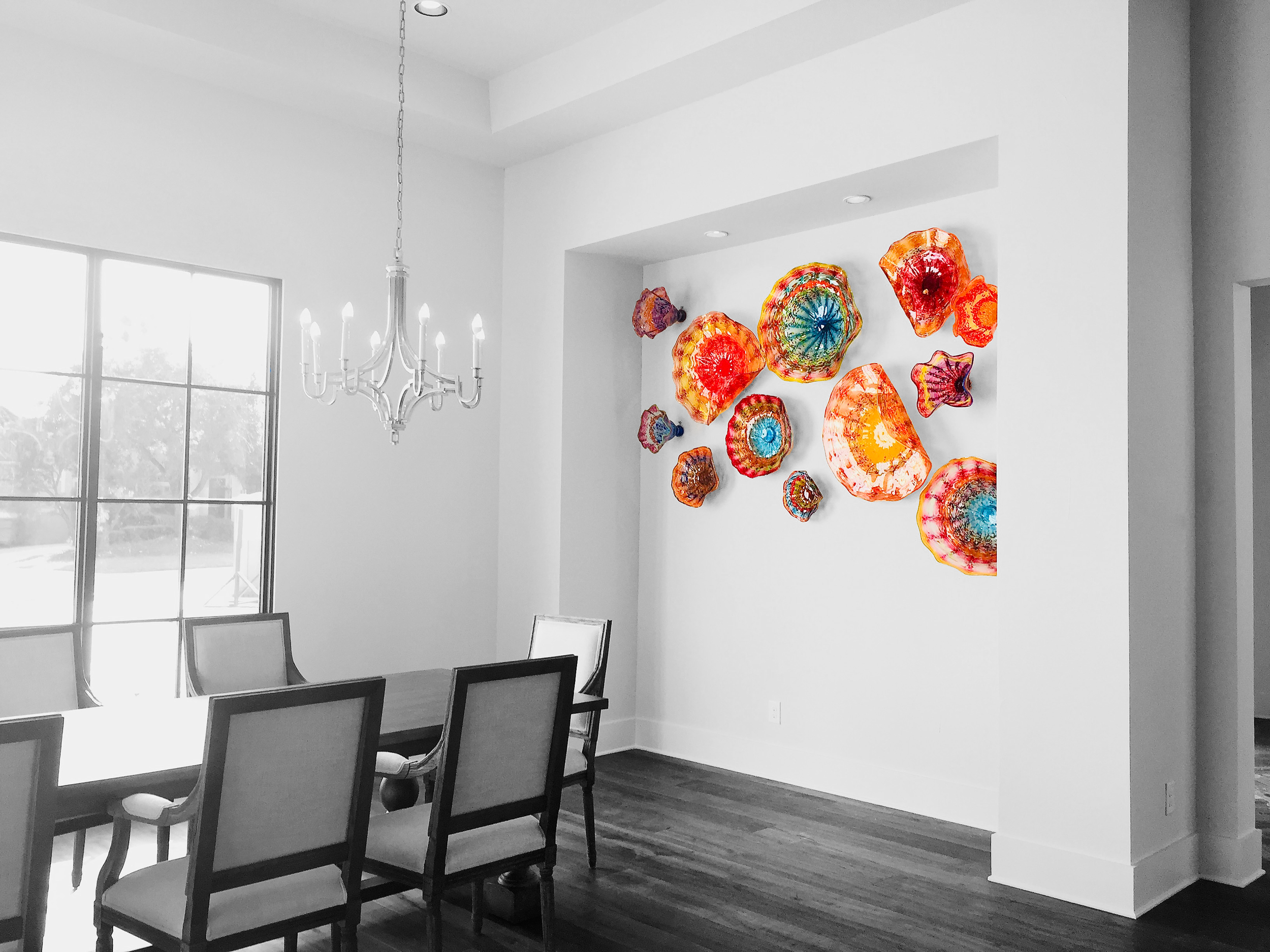 Contemporary dining room with black and white decor, a modern chandelier, and colorful glass art pieces on the wall.