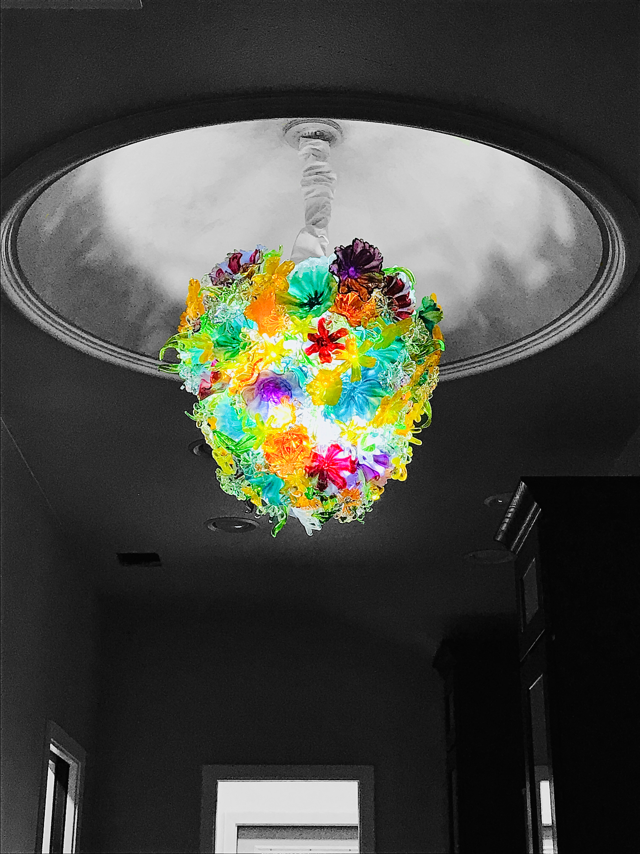 Colorful floral chandelier hanging from ceiling in black and white room.
