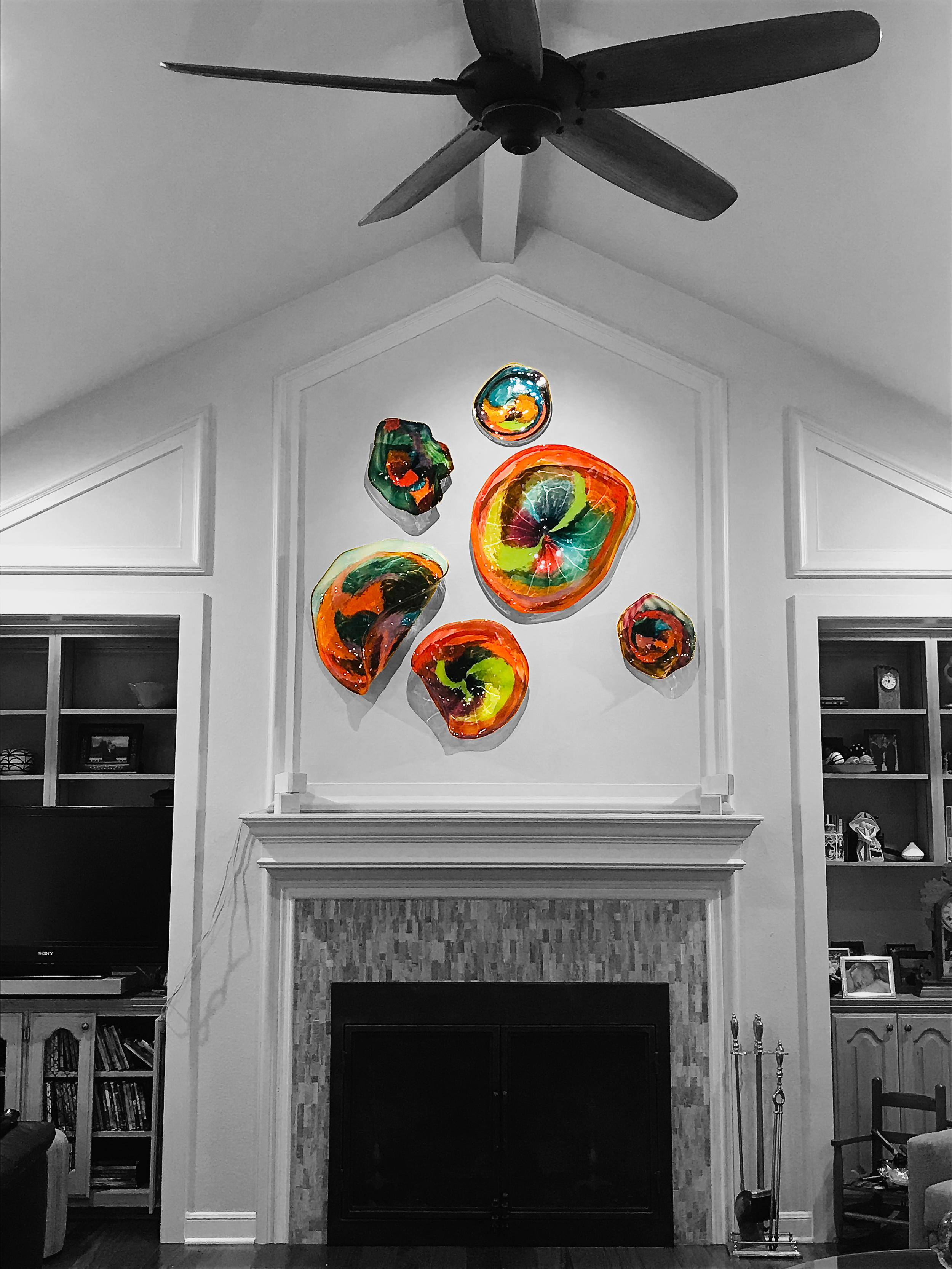 Colorful, abstract glass wall hanging above a fireplace in a living room with black and white decor.