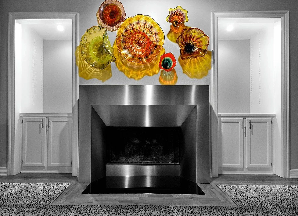 Colorful glass art sculptures above a modern fireplace in a monochrome room with built-in shelves on either side.