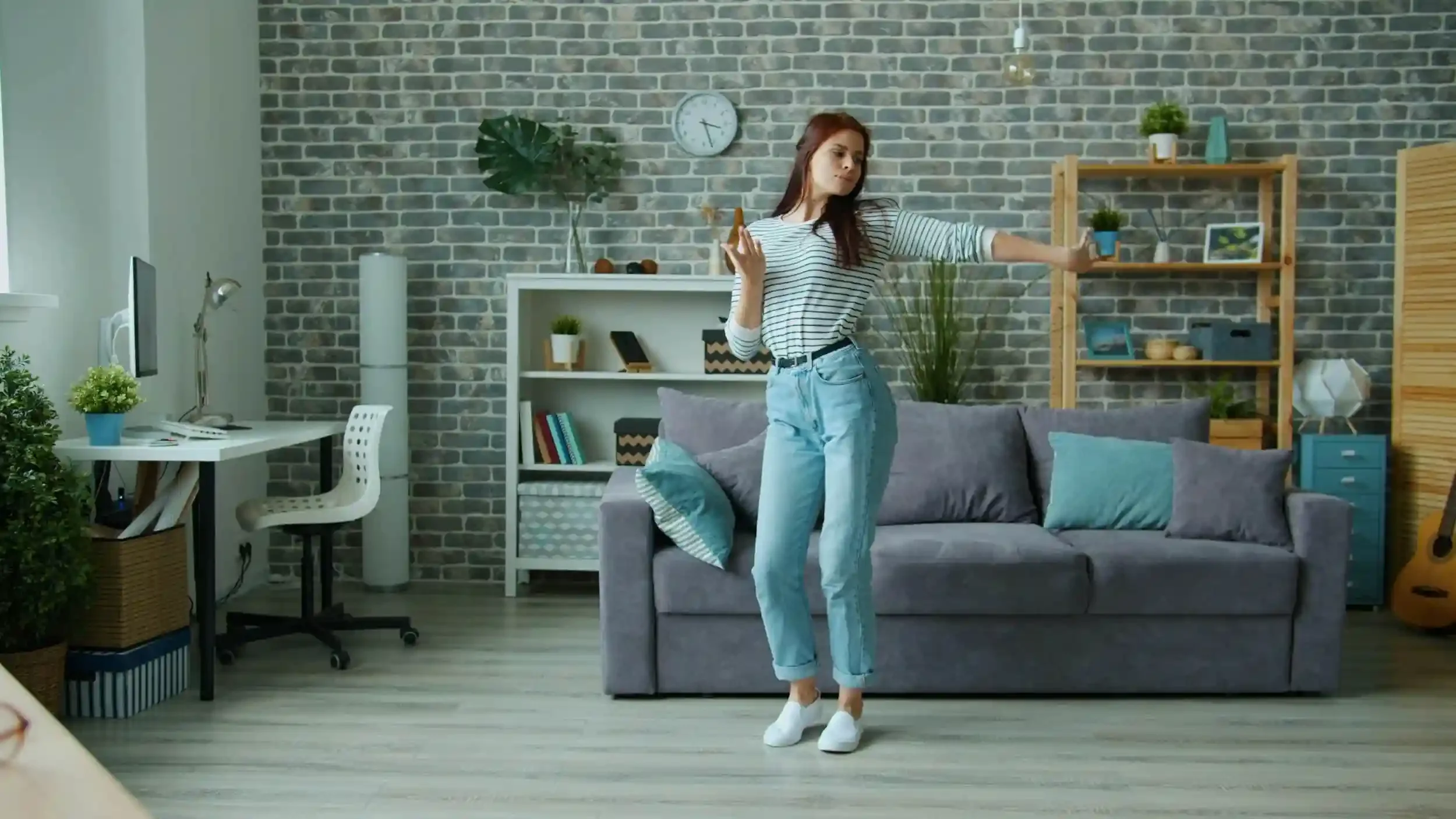 A woman dances happily in a modern living room, holding a phone with headphones on, surrounded by cozy decor and furniture.