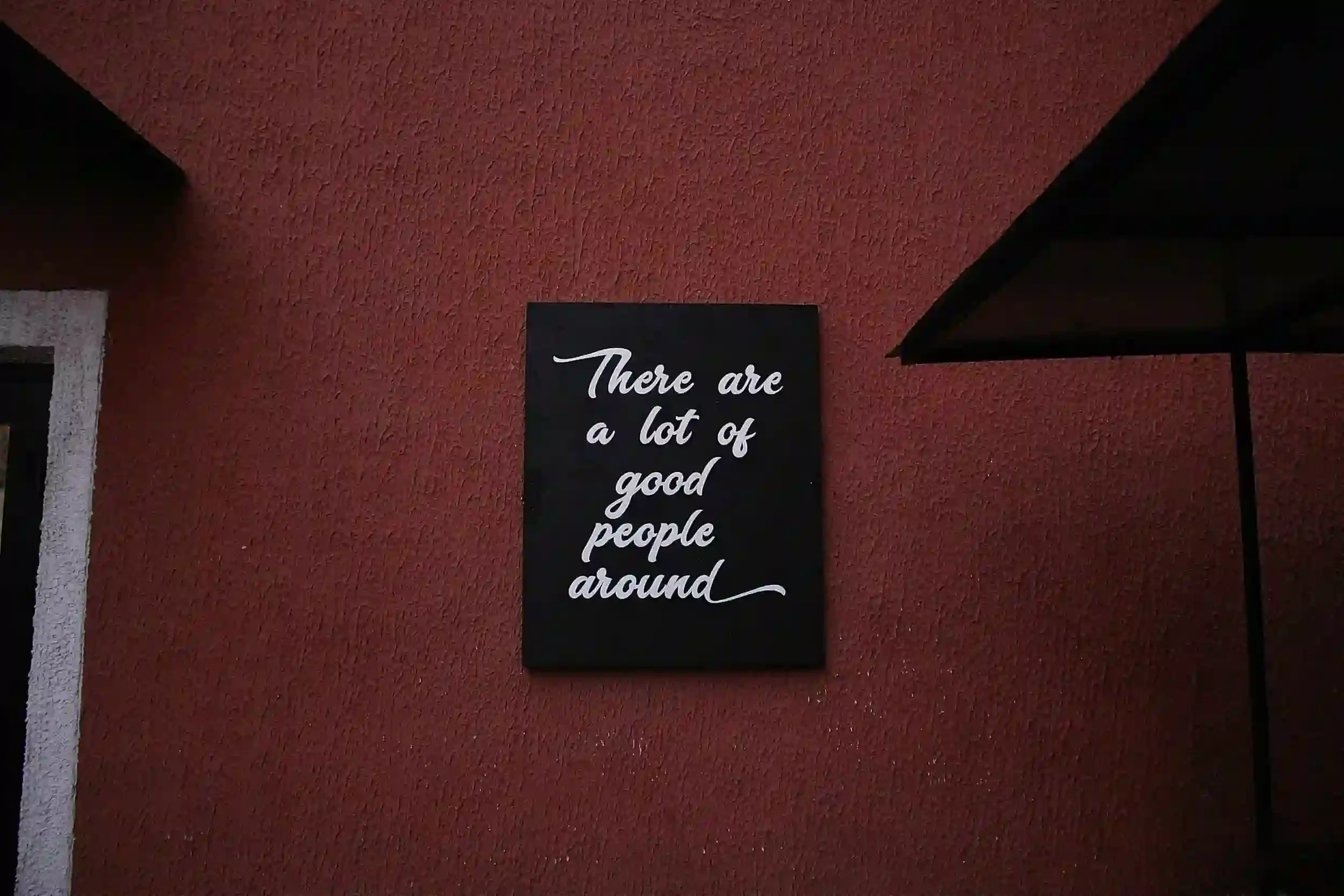 A black sign on a red wall reads, “There are a lot of good people around” in white cursive writing.