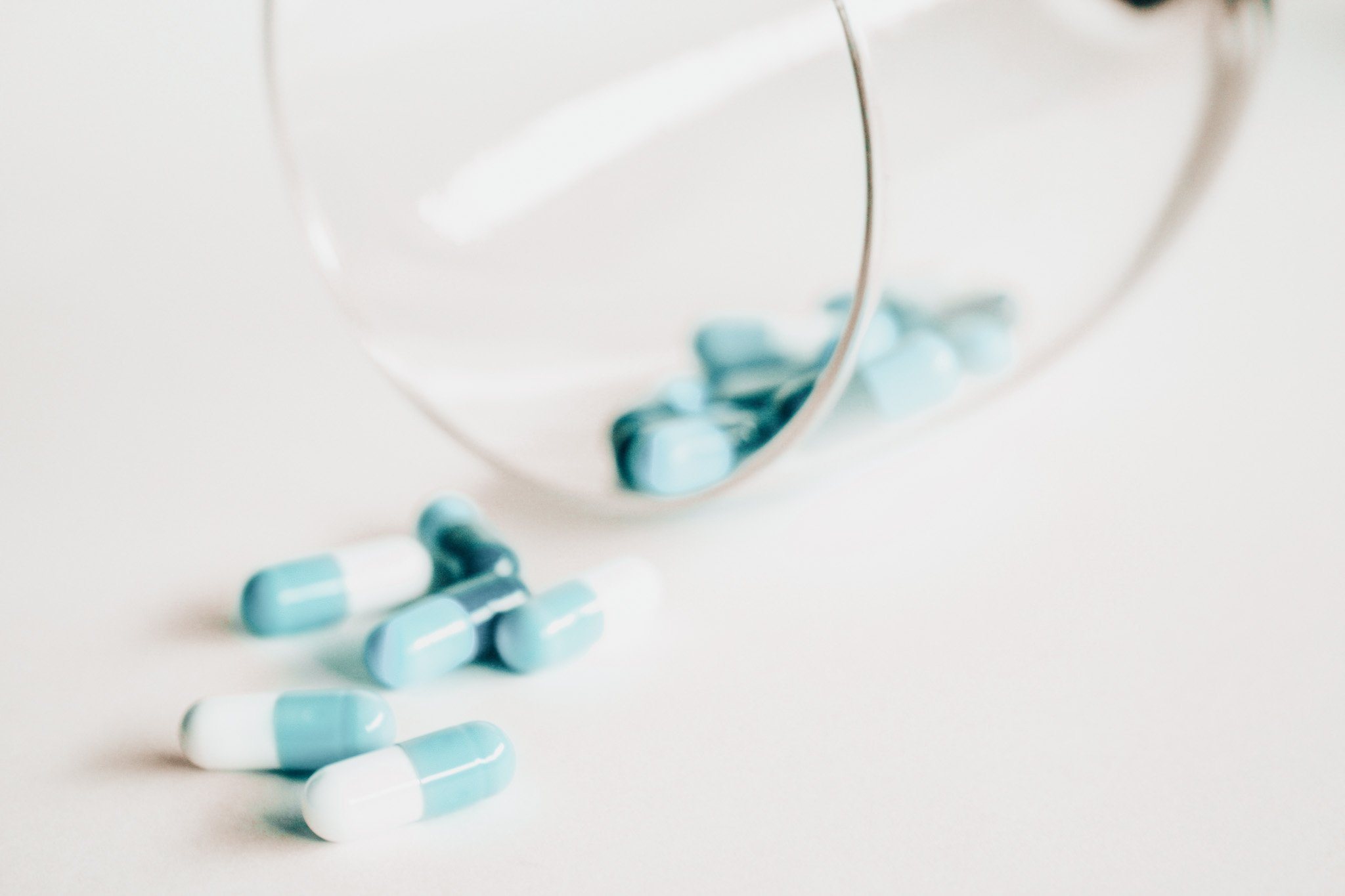 Blue and white capsules spilling from a glass bottle onto a white surface.