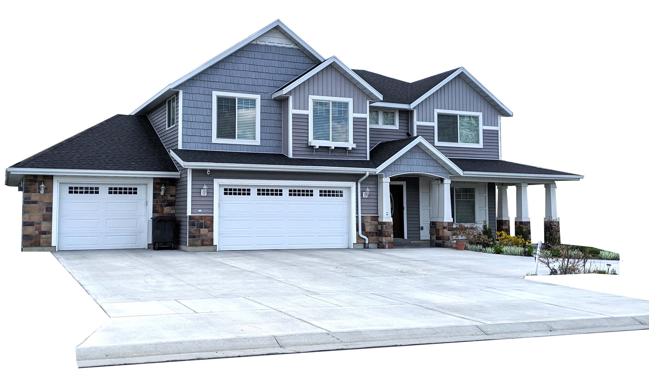 A two-story house with gray siding, white trim, and a front porch with columns, featuring a concrete driveway, a landscaped garden, and a garage with white doors.