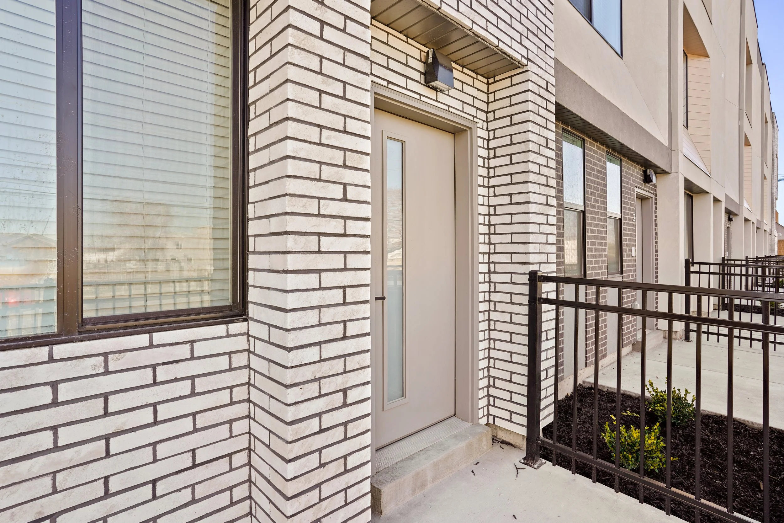 A SUR17 townhome front entry with white brick, a glass-panel door and a small fenced yard