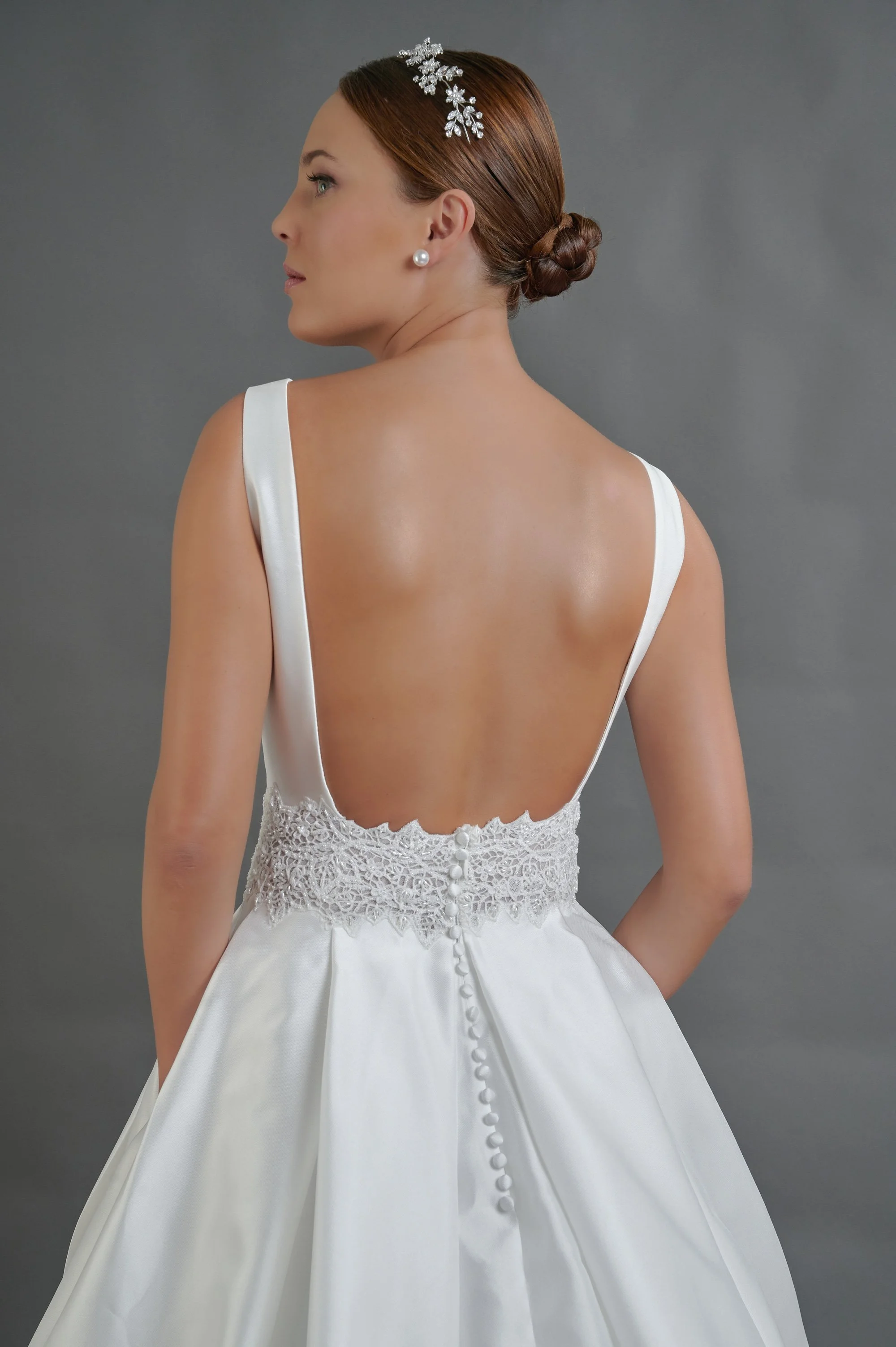 Novia con el vestido Quintana de Bridenformal, princesa de satén liso con cinturón de pedrería, vista frontal con cola.