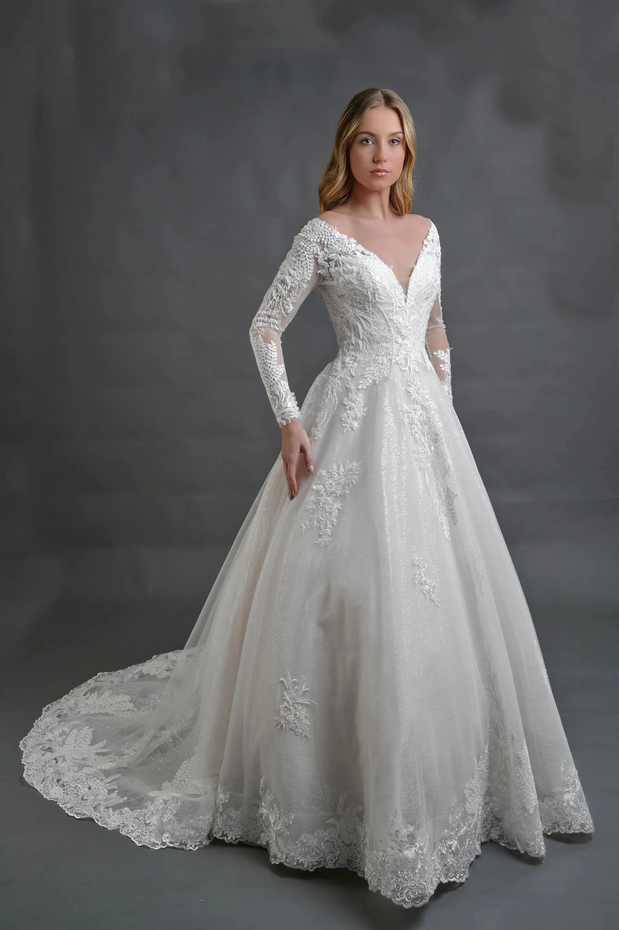 Novia con el vestido Basilea de Bridenformal, princesa de tul con brillo y mangas largas de encaje, vista frontal con cola.