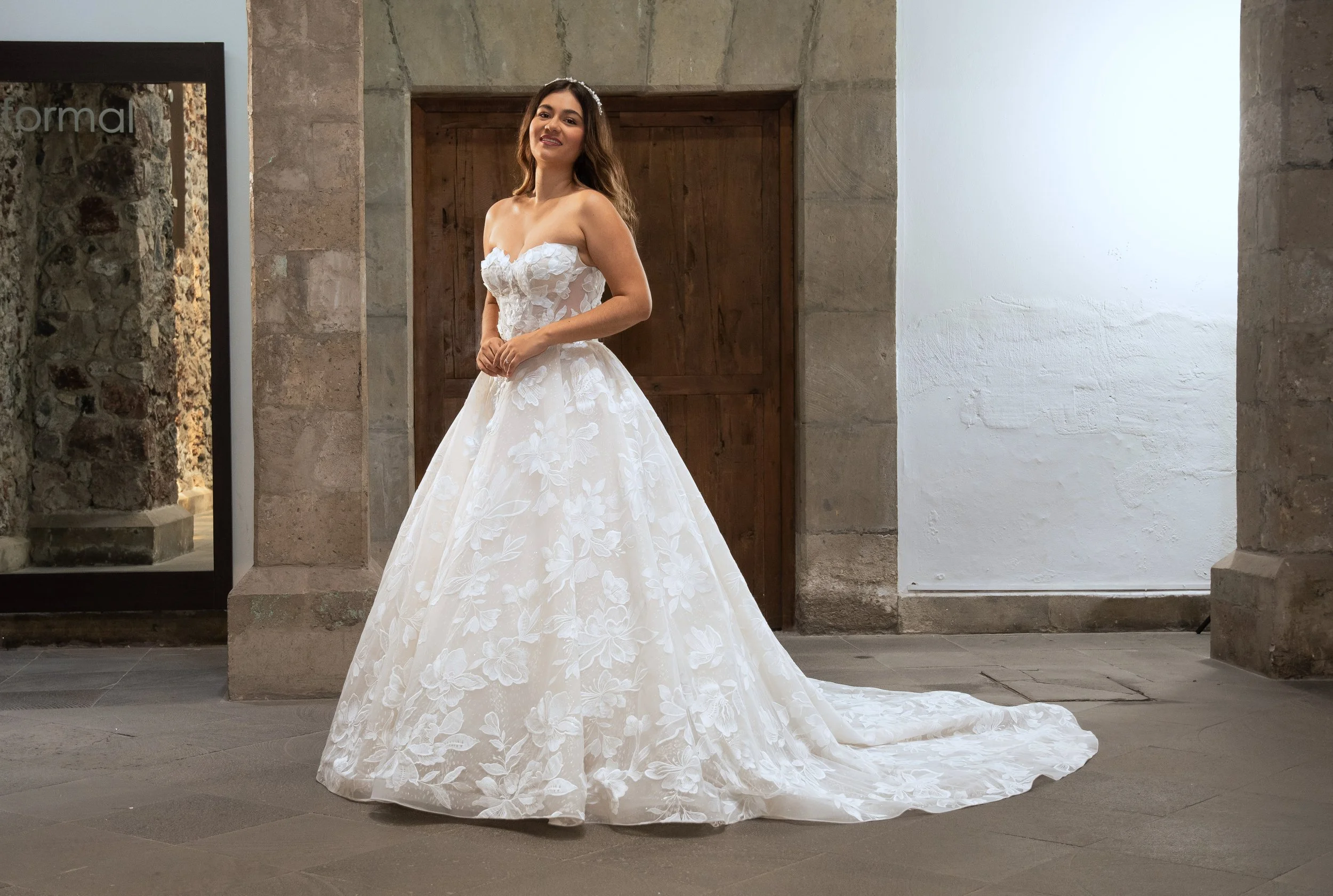 Vestido de novia Lupita de frente con la falda floral de línea A y la cola extendida.