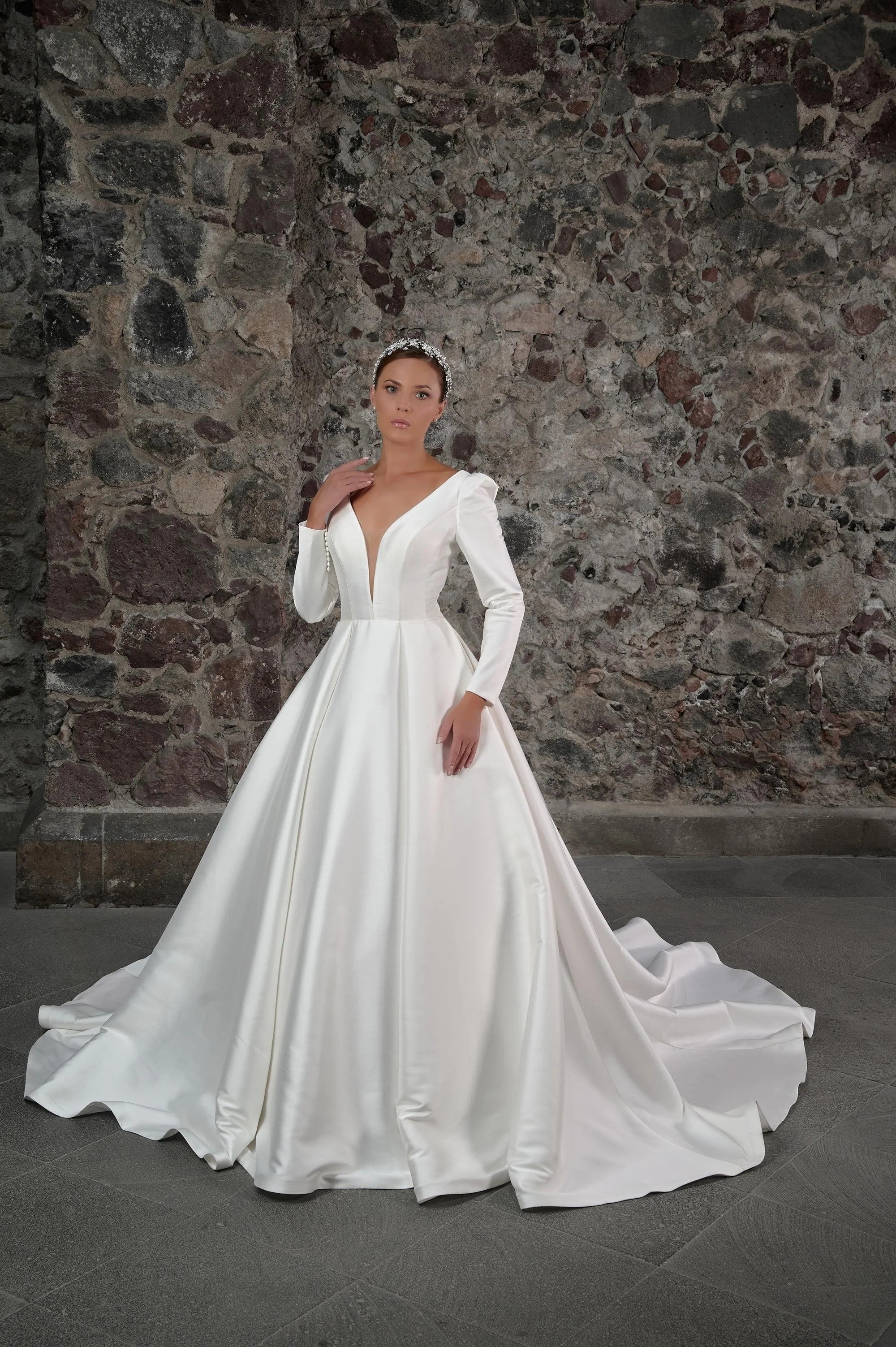 Novia con el vestido Celeste de Bridenformal, satén minimalista con mangas largas y escote en V, vista frontal con cola.