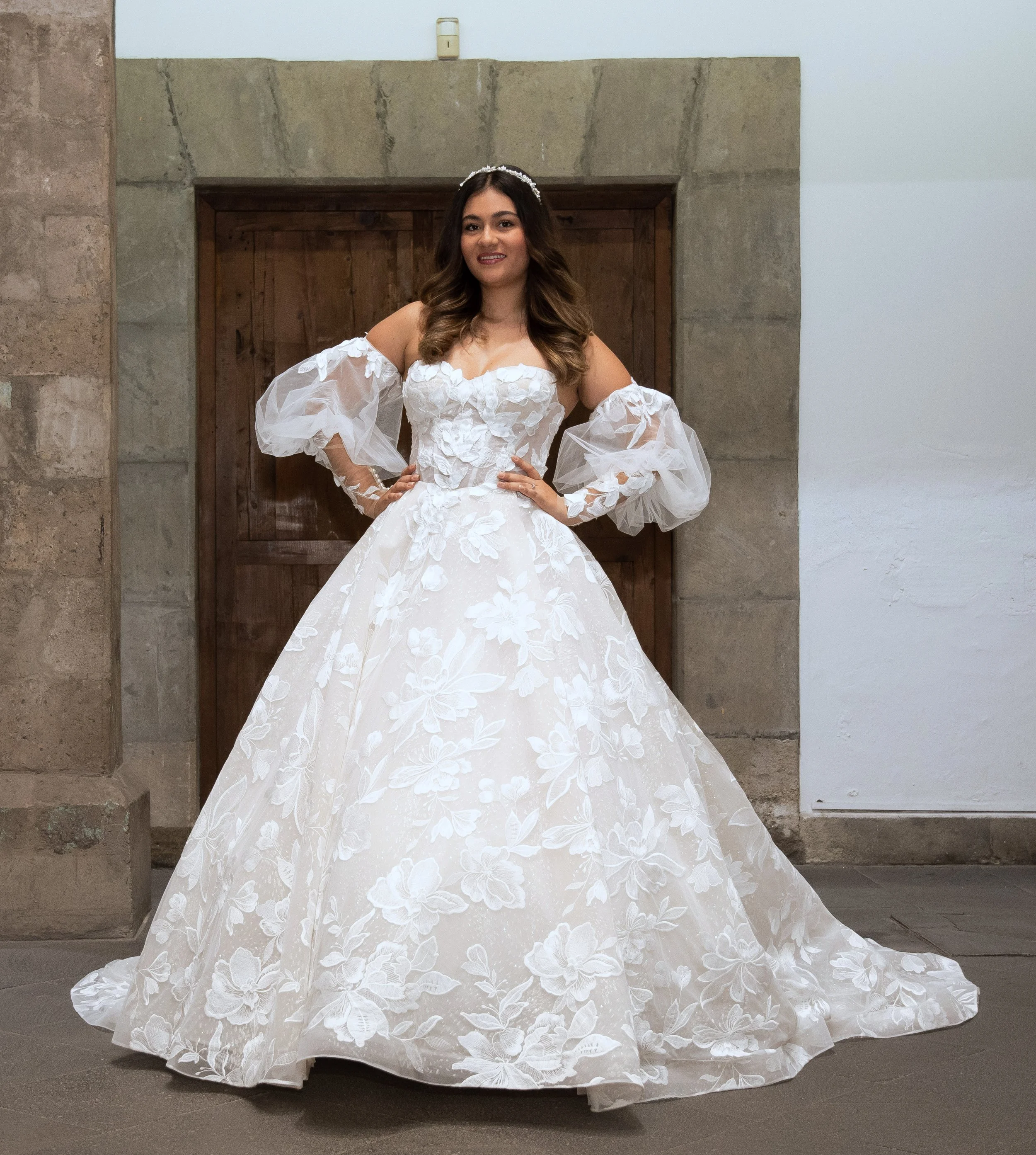 Novia con el vestido Lupita de Bridenformal, línea A con flores en relieve y mangas caídas, vista frontal completa.