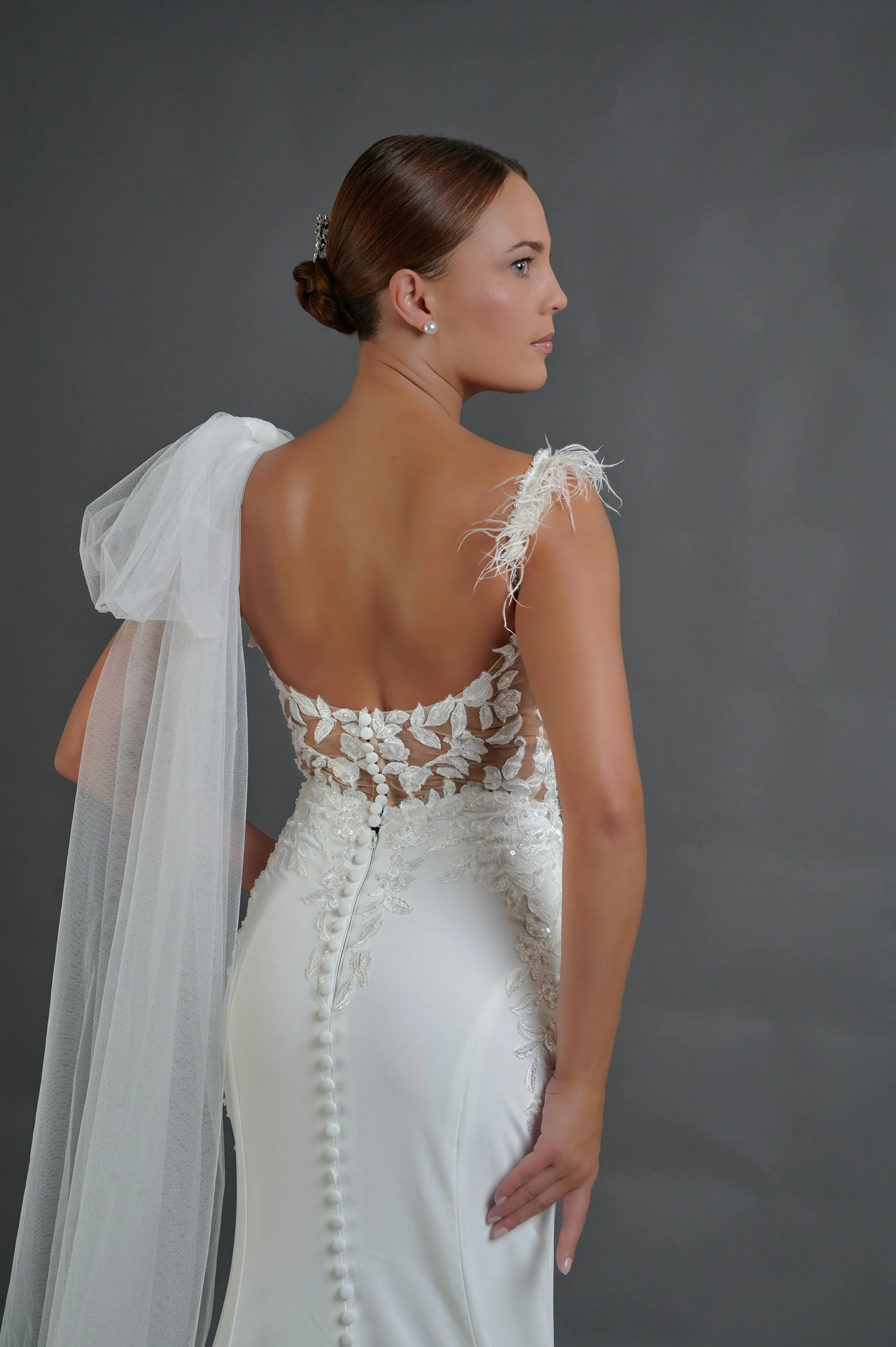 Detalle de la espalda descubierta del vestido Baran con corpiño de encaje de ilusión, botones forrados y tirante de plumas.