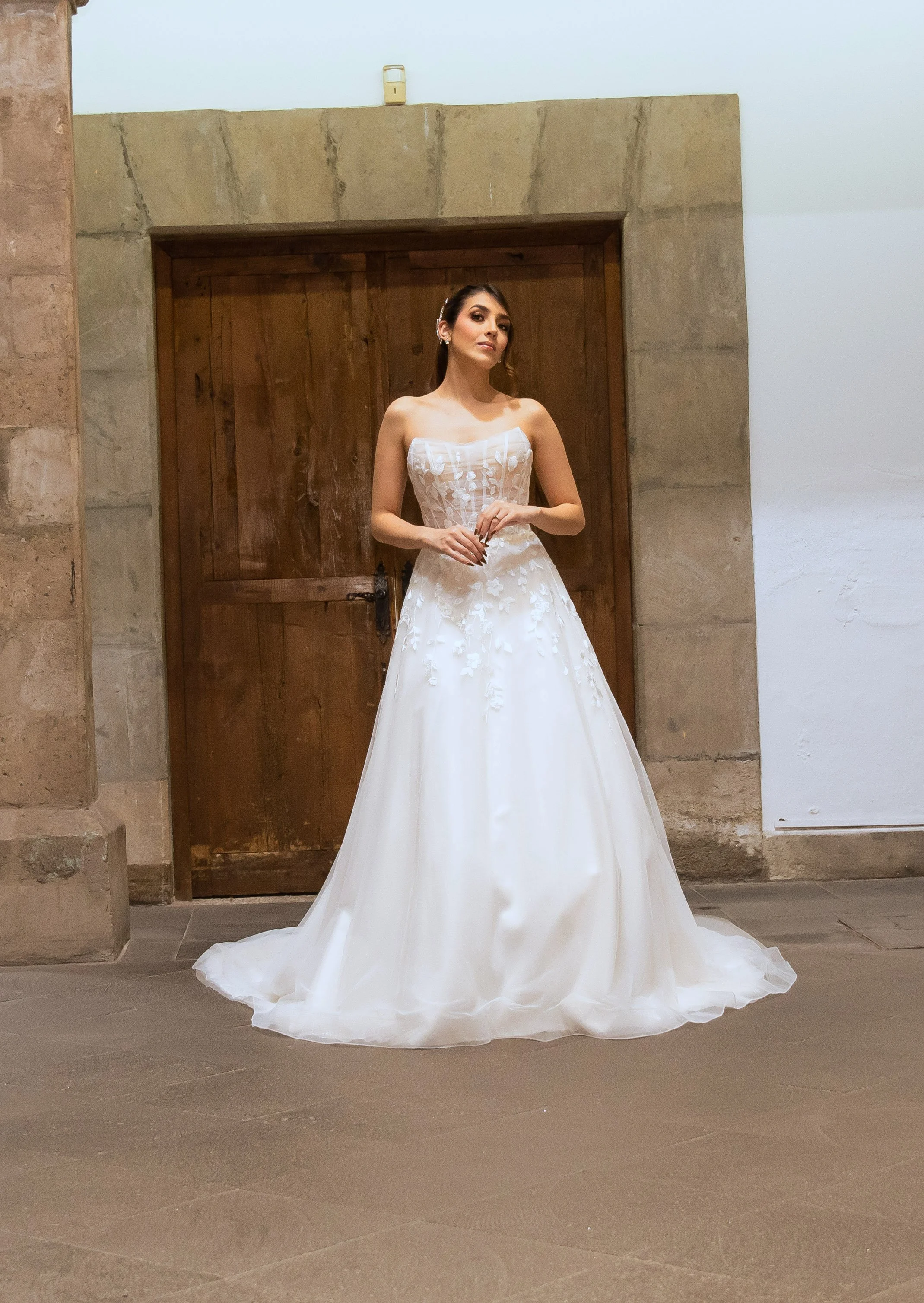 Novia con el vestido Lujo de Bridenformal, línea A de tul con corsé transparente y flores en relieve, vista frontal completa.