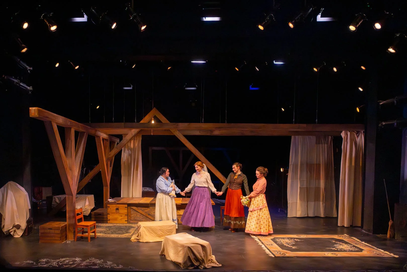 Four women hold hands in an attic.