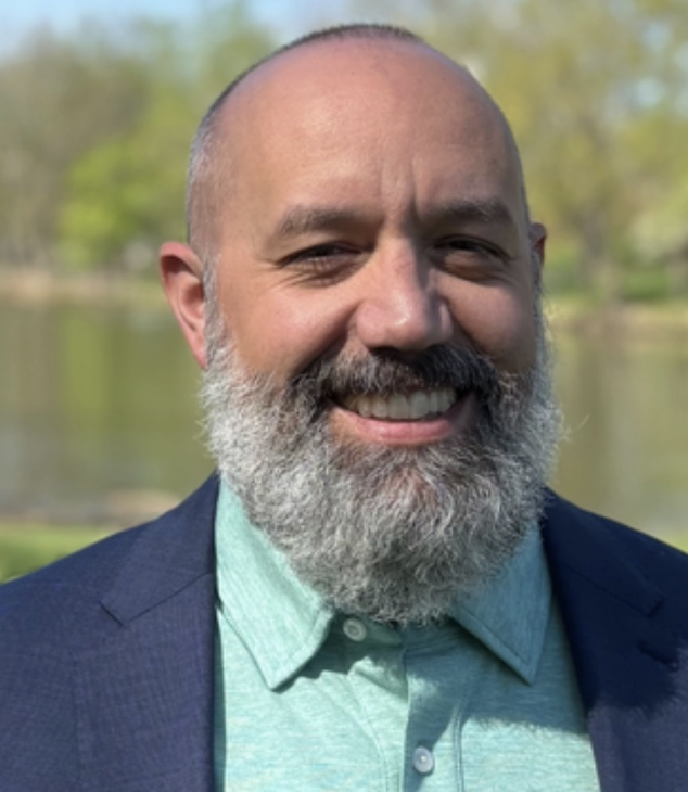 Bloomsburg Mayor Justin Hummel, a white man with a salt and pepper beard, stands in front of a lake.