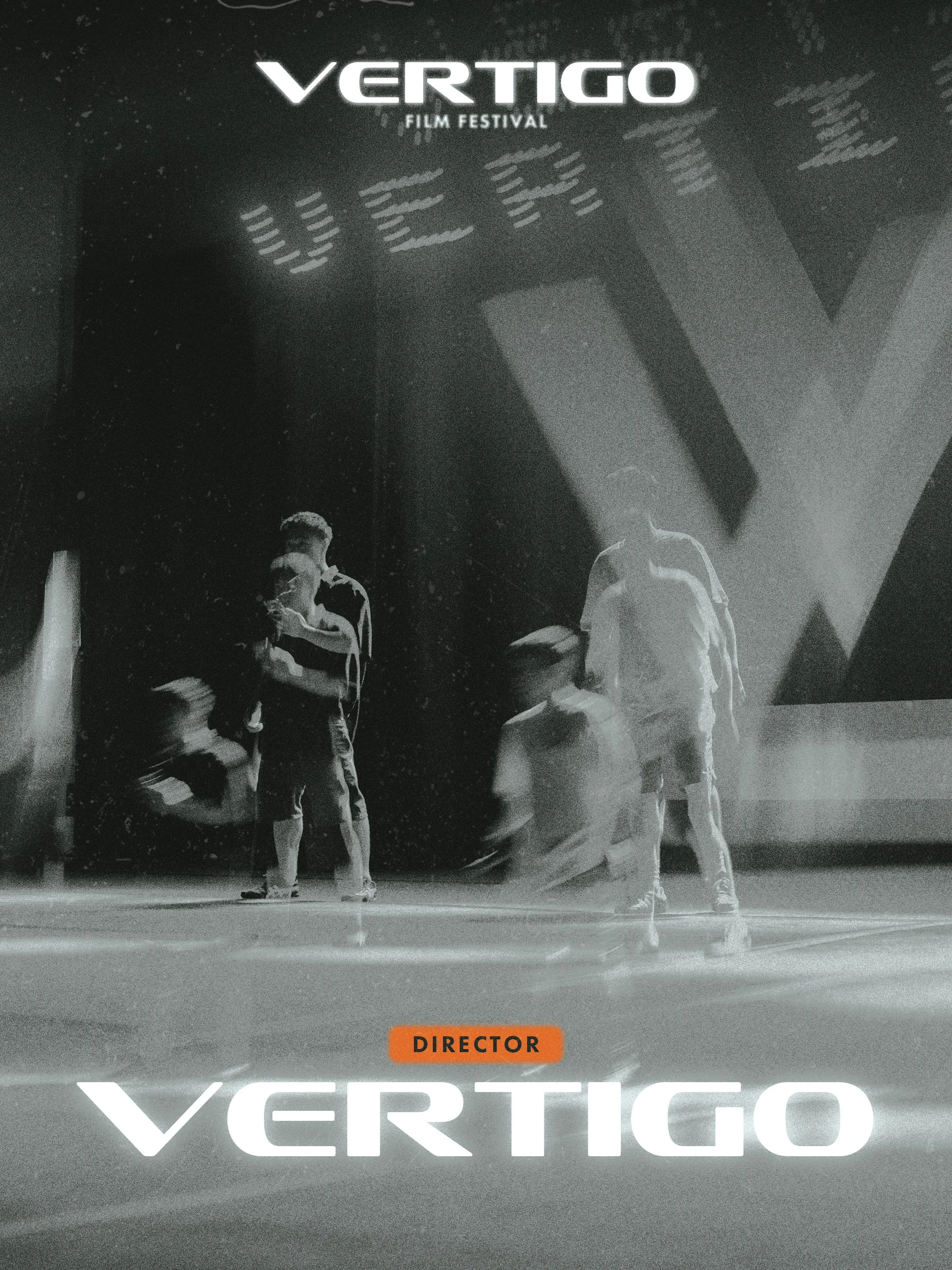 Black and white photograph of a stage at a film festival with the words "VERTIGO FILM FESTIVAL" displayed at the top. Four people are present on the stage, with one sitting and three standing. A bright light source creates a halo effect around the standing individuals. An orange label reading "DIRECTOR" is at the bottom of the image.