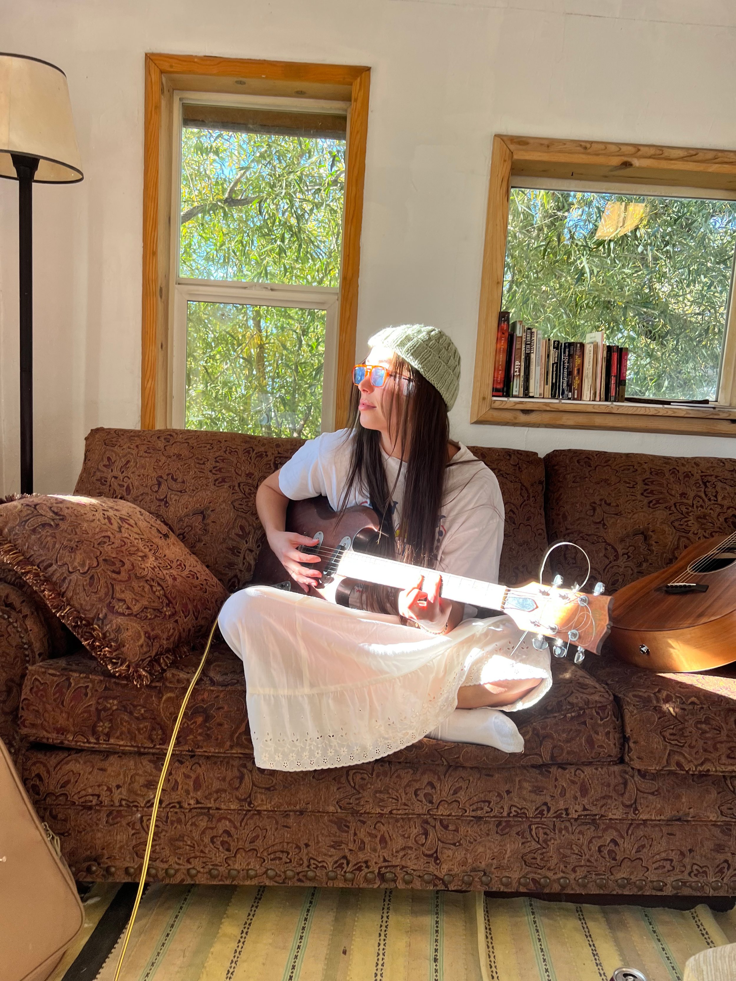A woman sitting on top of a yellow skid steer loader in a desert landscape, with a man sitting inside the loader, wearing a beanie and jacket.