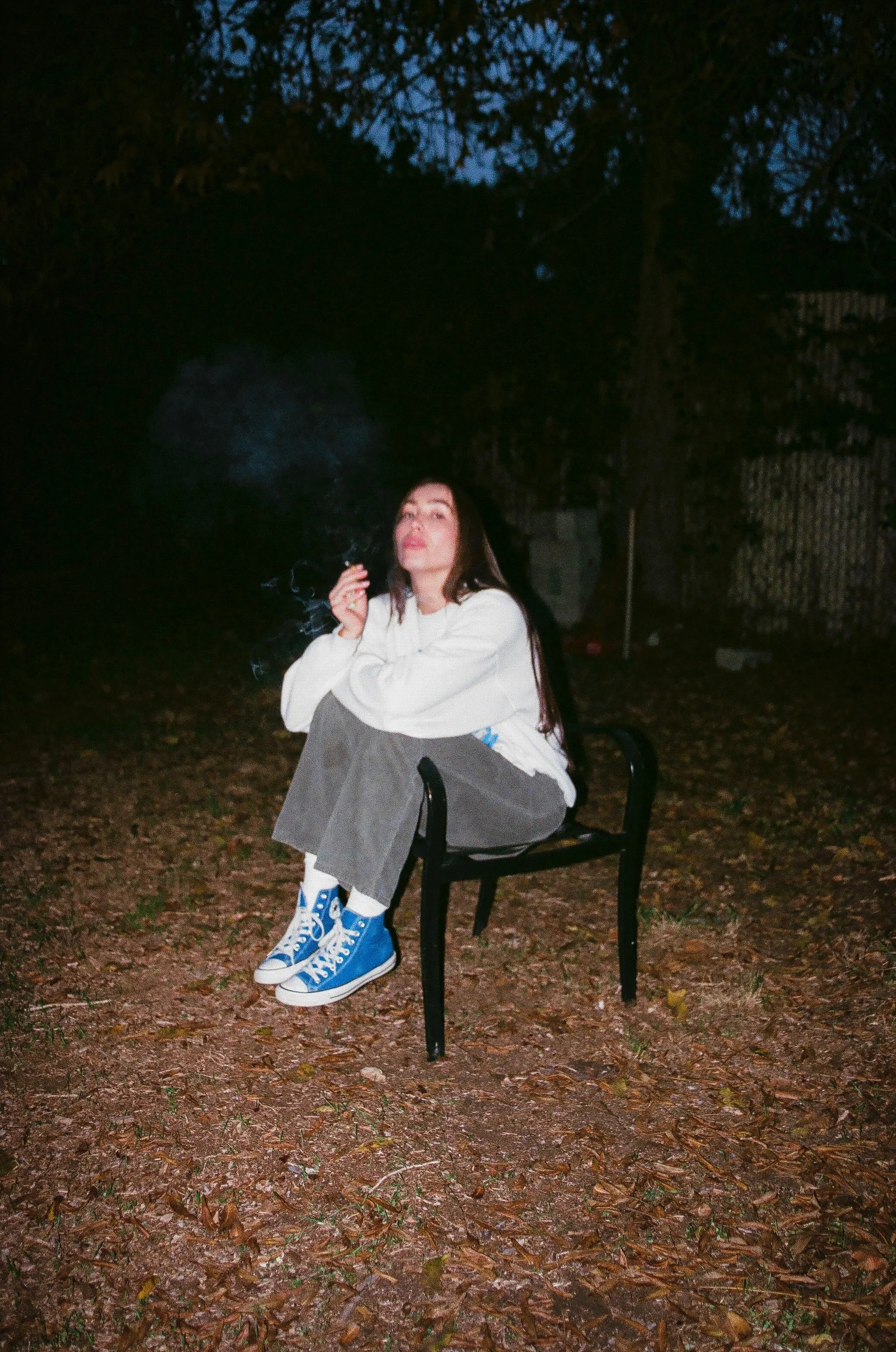 A woman sitting on the floor, playing an electric guitar, smiling and looking upwards, captured in black and white.