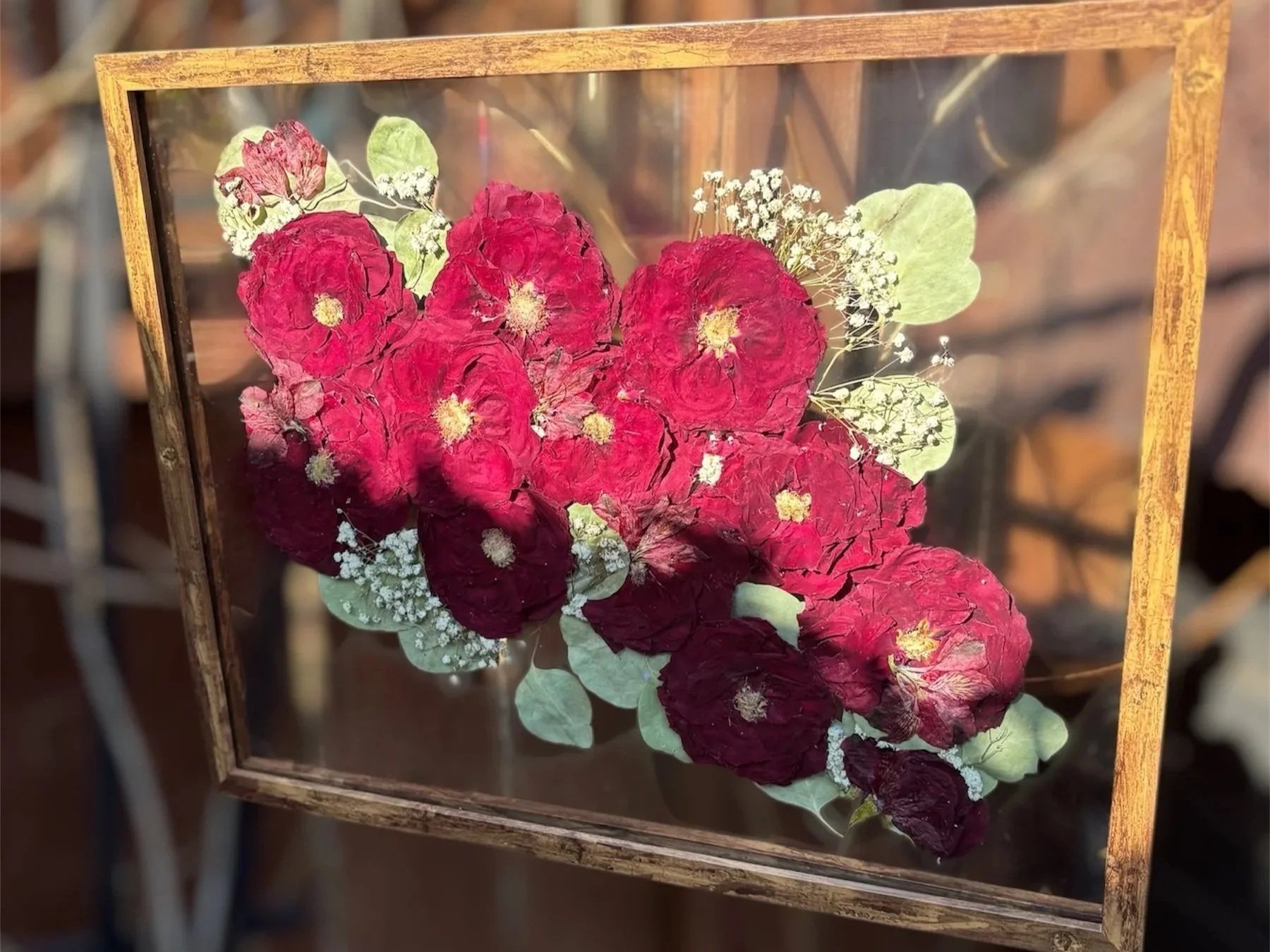 Pressed red and white flowers displayed inside a wooden and glass frame. Wedding bouquet pressed flower frame.