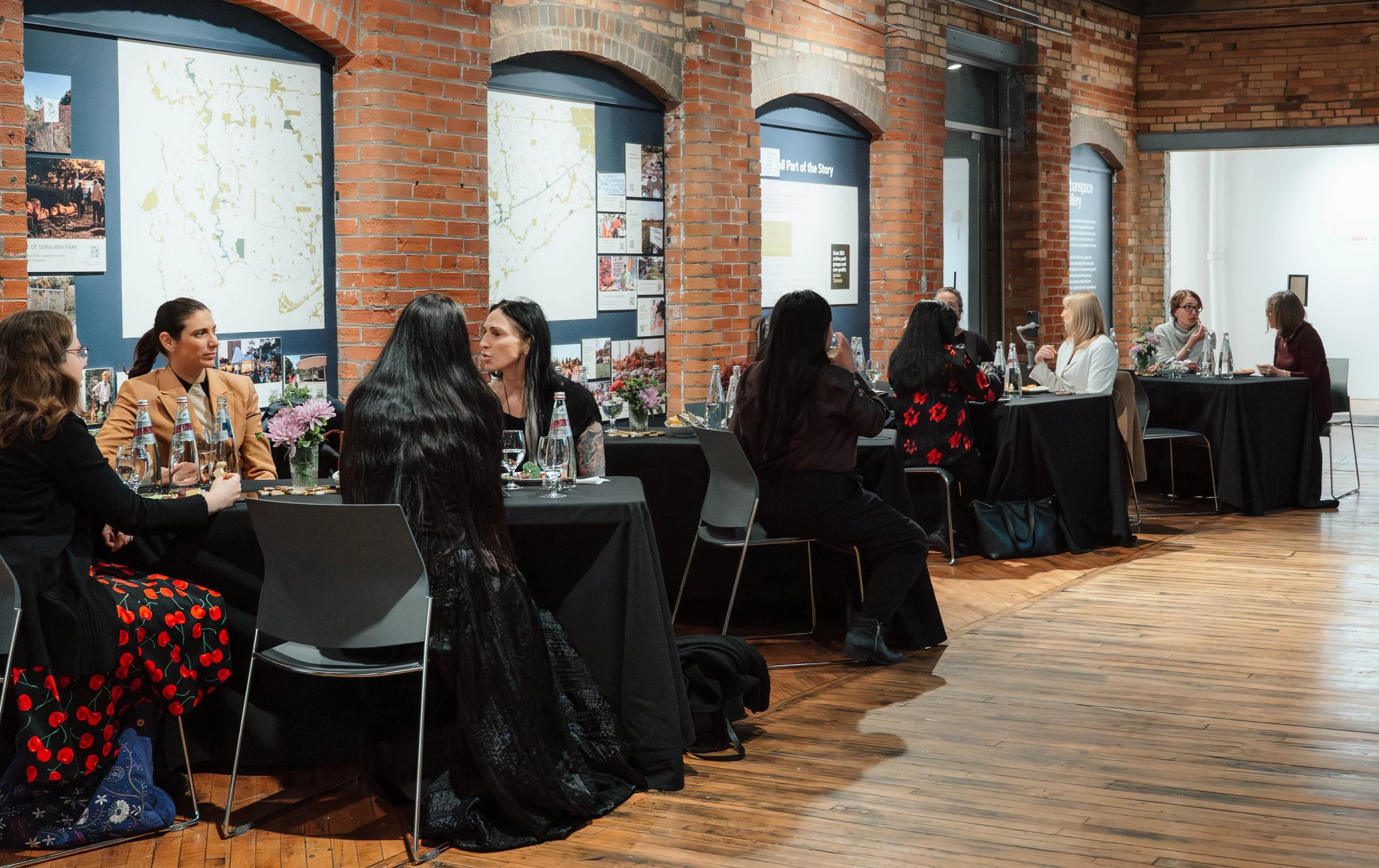 Women participating in a discussion or workshop during a conference in a brick-walled room with photographs and maps on the walls.