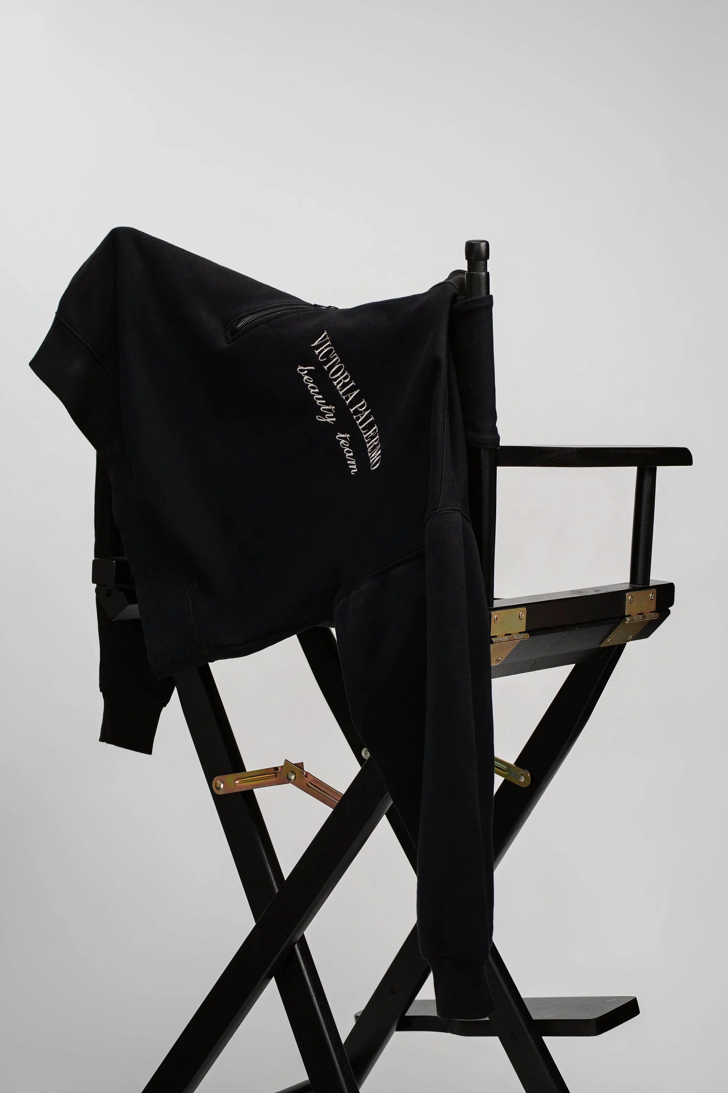 A black director's chair with a black Victorina Paladino jacket draped over the backrest against a plain white background.